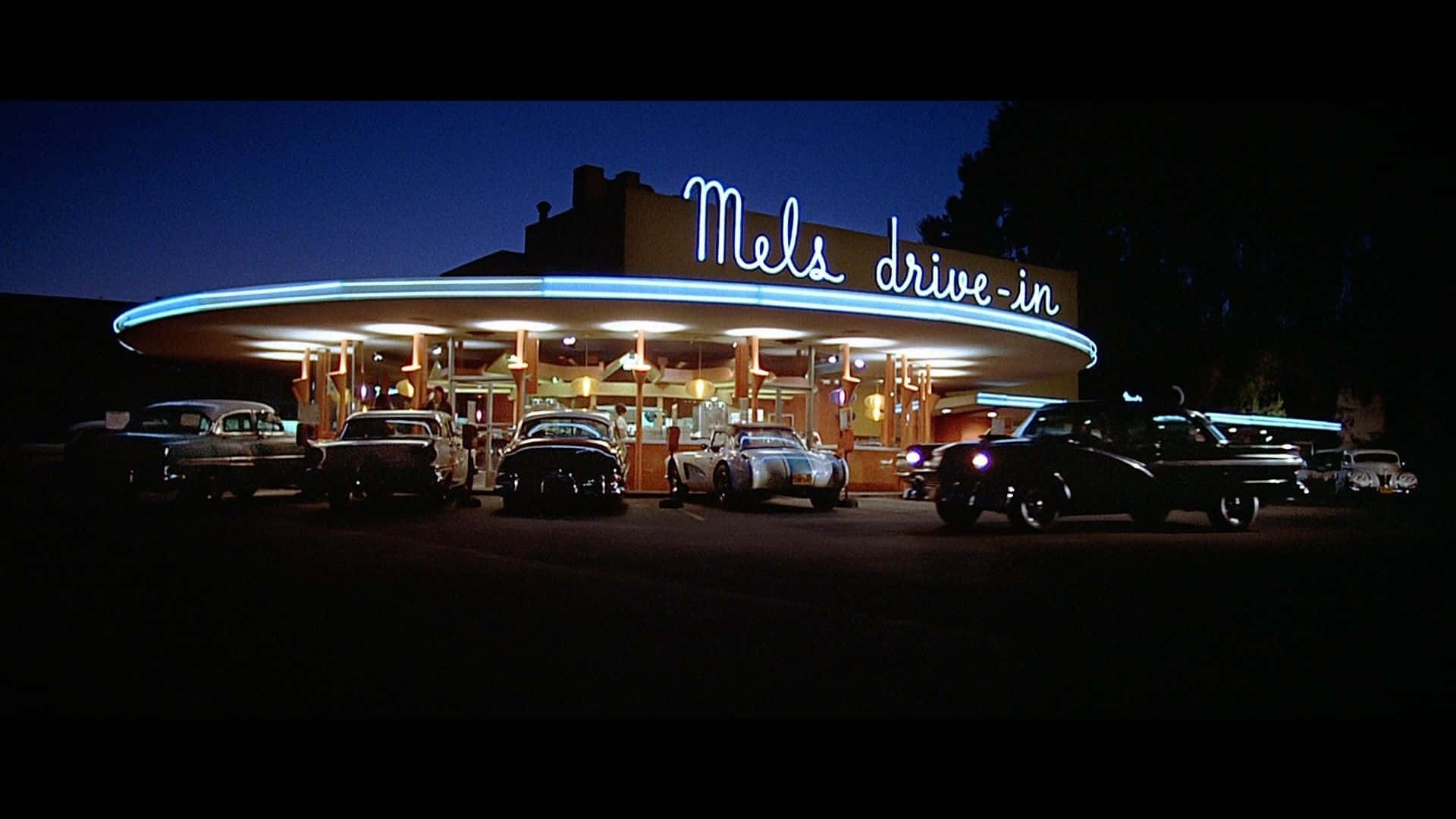 經典汽車停泊在夜晚霓虹燈照亮的1950年代得來速餐廳。