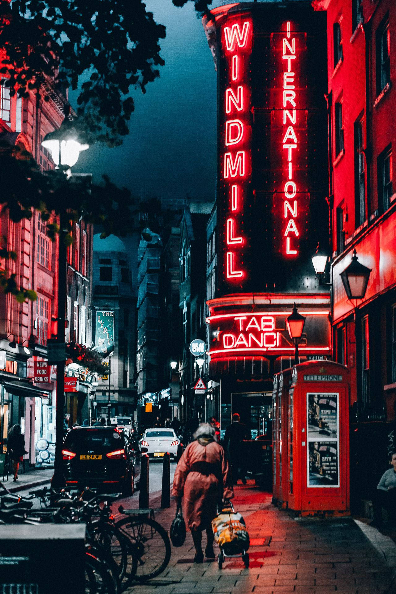 復古風格「紅色城市」 壁紙 — 一個孤獨的身影在夜晚沿著倫敦一條狹窄的街道行走，被風車劇院充滿活力的紅色霓虹燈招牌照亮。