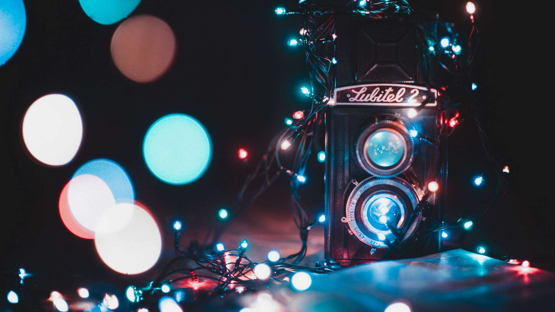 復古風格散景燈光 壁紙 — 復古Lubitel 2相機包裹在閃爍的仙女燈中，背景黑暗，帶有彩色散景圓圈。