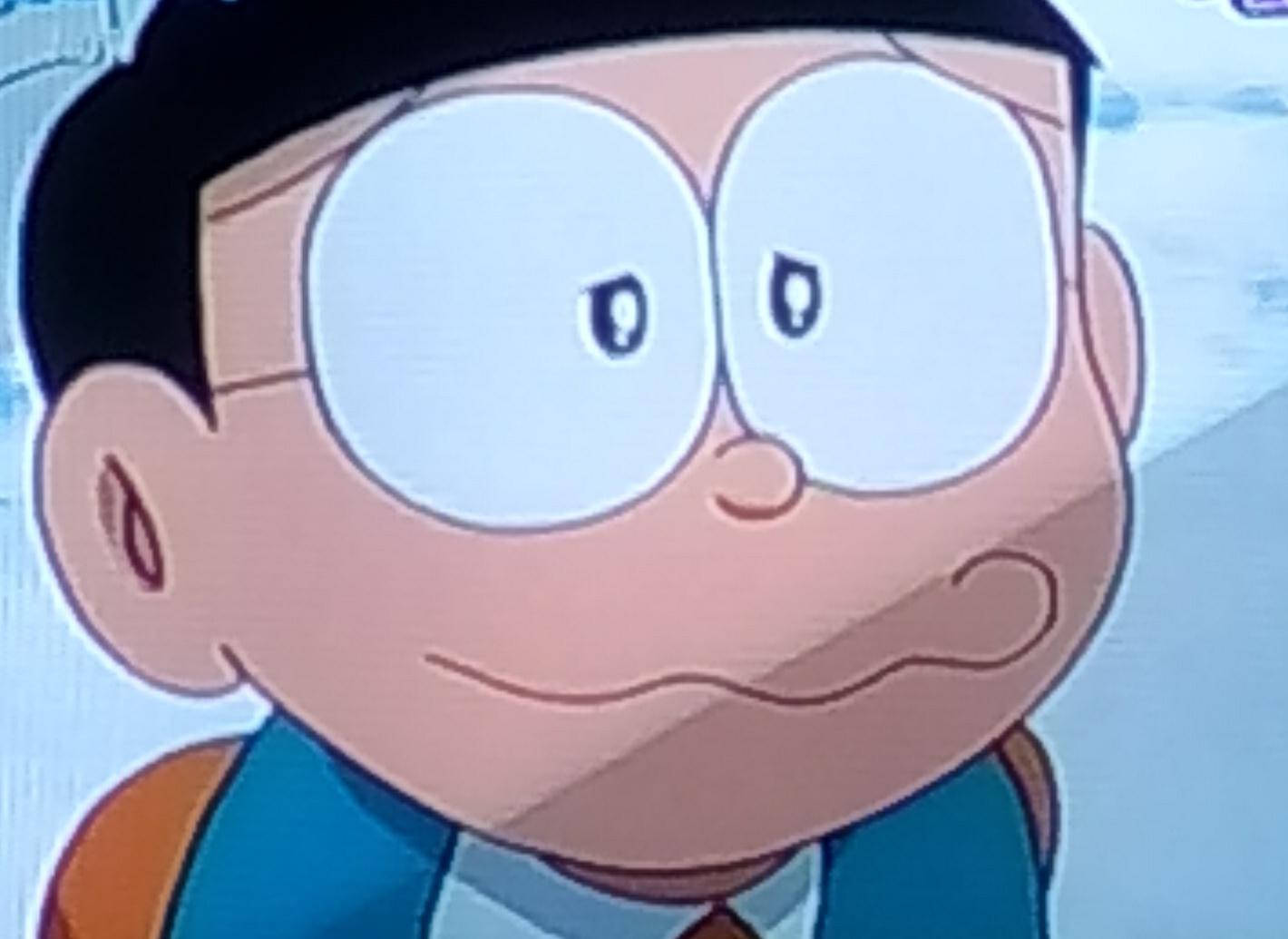 戴著大圓眼鏡、露出微妙笑容的動漫男孩，身穿藍色背心。
