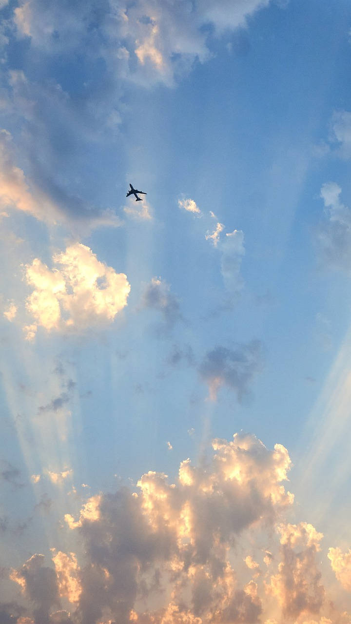 一架飛機在夕陽天空下飛行，伴隨著金色雲彩和陽光。