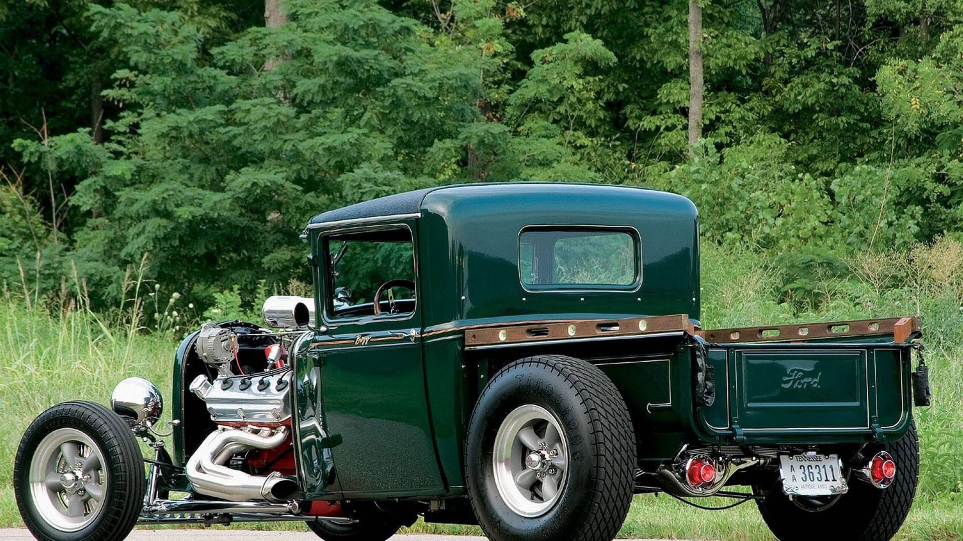 綠色復古福特 hot rod 貨車，帶有鍍鉻引擎，停泊在草地森林中。
