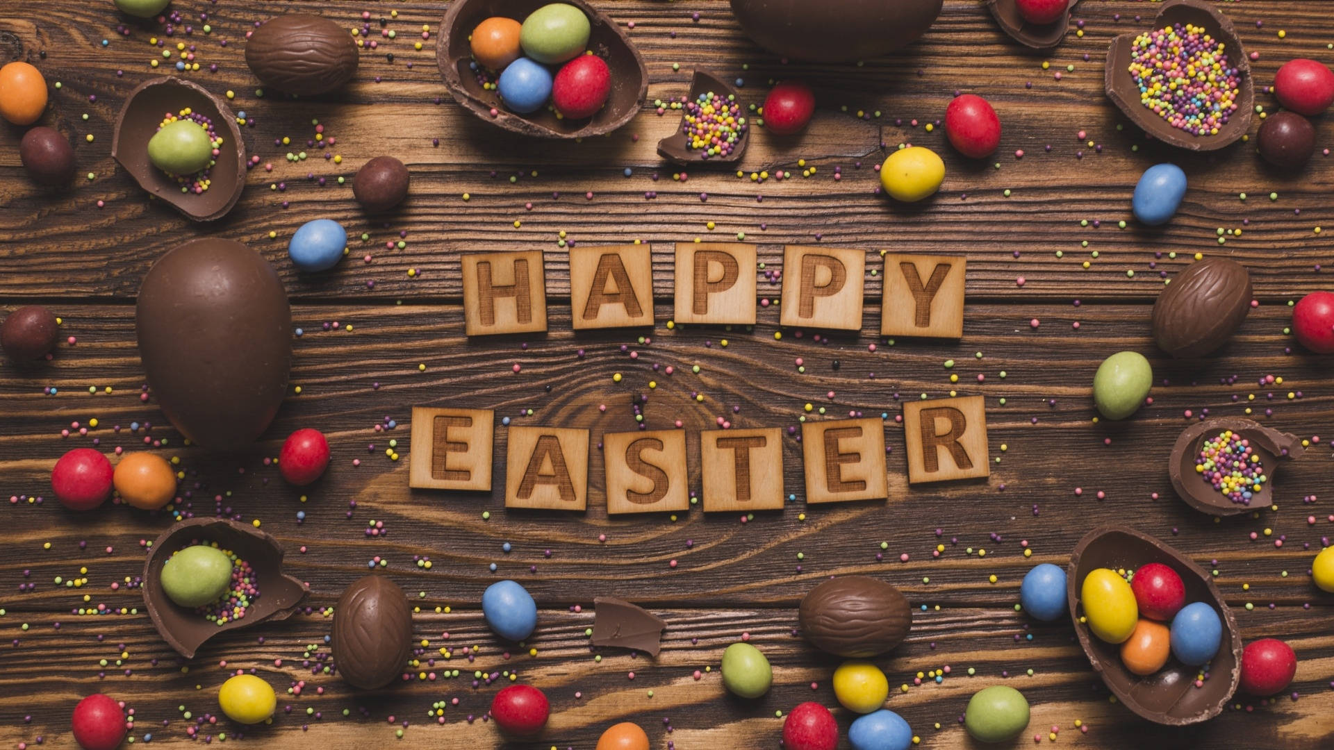 木製字母塊拼出的Happy Easter被朱古力蛋和色彩繽紛的糖果包圍在木頭上。