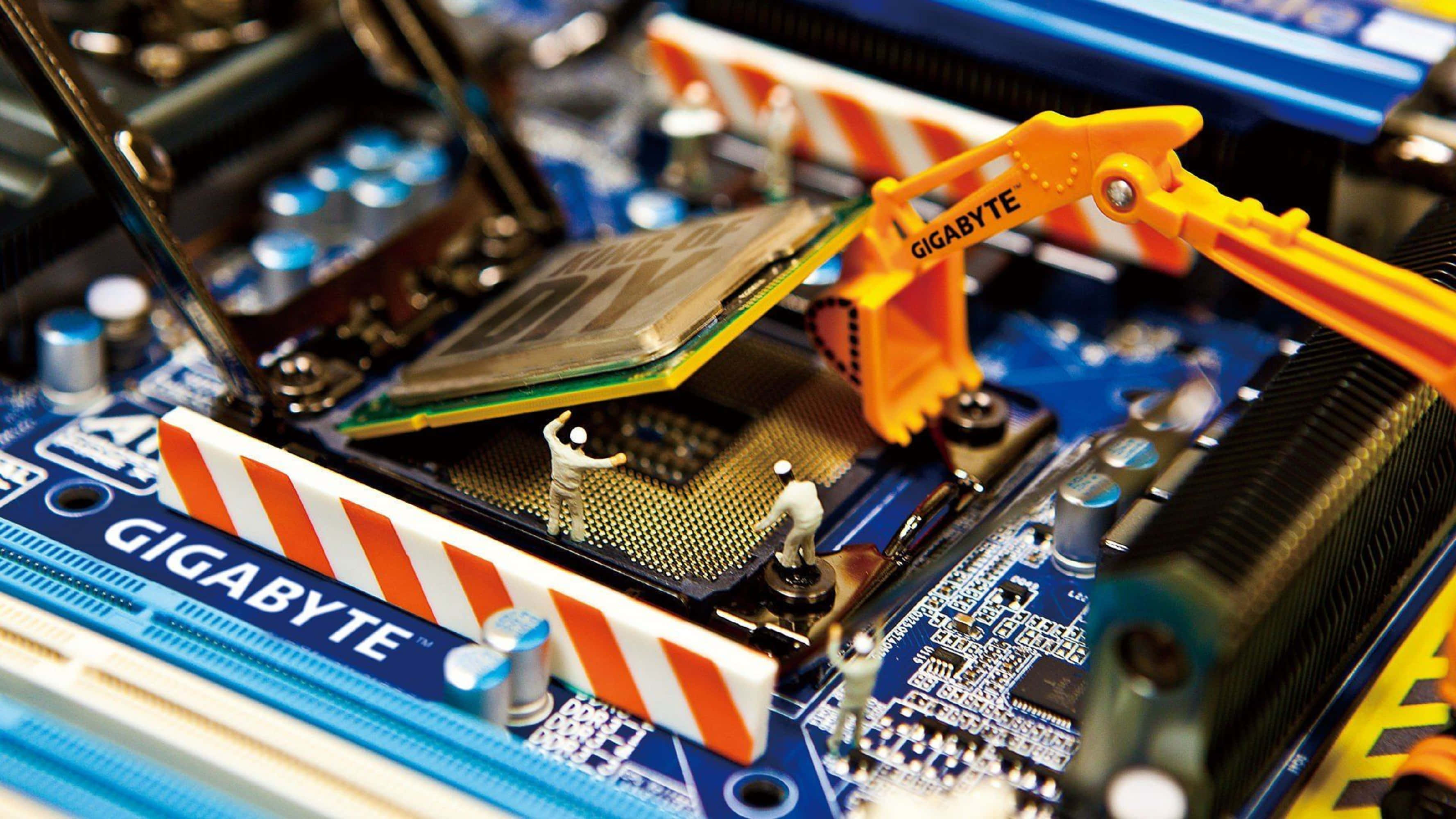 4K Processor 桌布 壁紙 — 微型建築工人使用迷你起重機將CPU安裝到被安全護欄包圍的藍色Gigabyte主機板上。