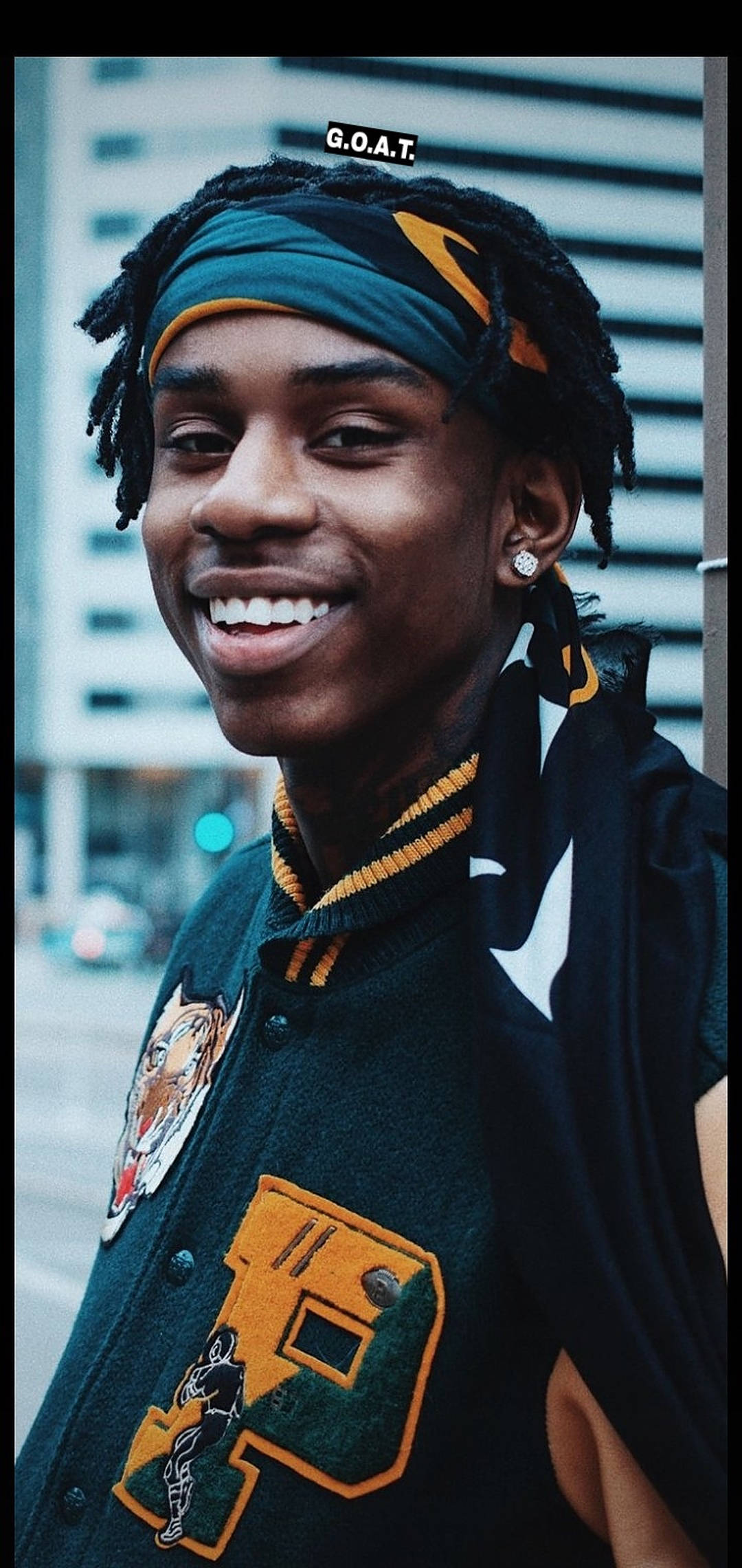 微笑 Polo G 校隊夾克 壁紙 — 一位年輕男子留著辮子頭和頭帶，穿著帶有老虎和籃球補丁的校隊夾克，燦爛地微笑。