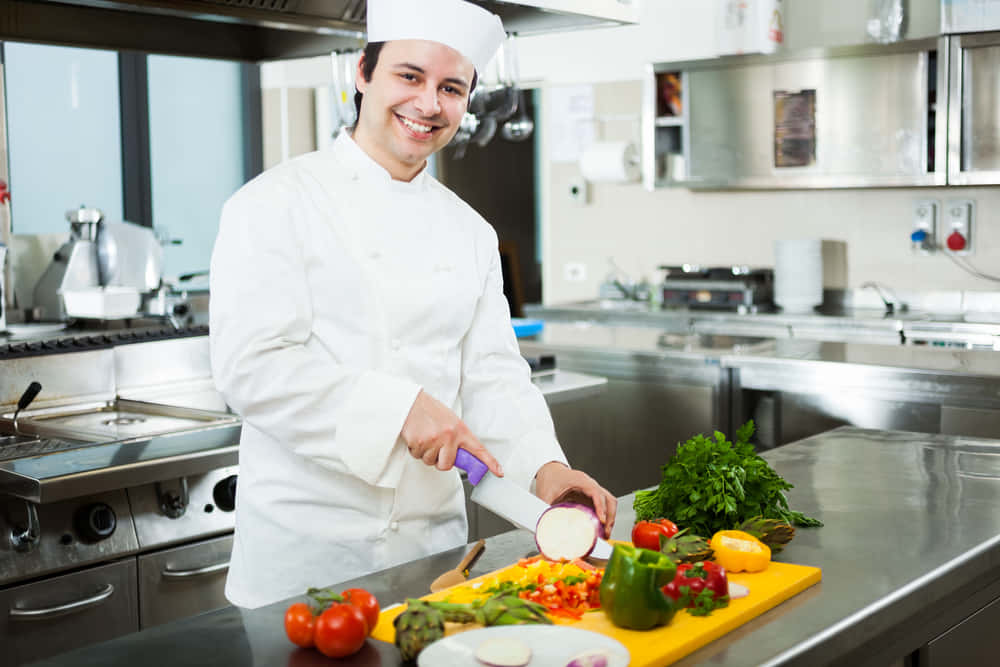 廚師在專業廚房裡切茄子，旁邊有色彩繽紛的蔬菜。