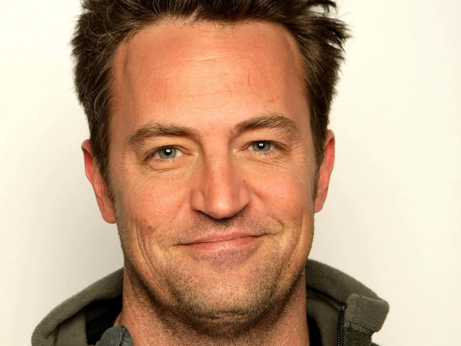matthew perry 桌布 壁紙 — 微笑男子藍眼睛鬚根特寫肖像，背景為純白色。