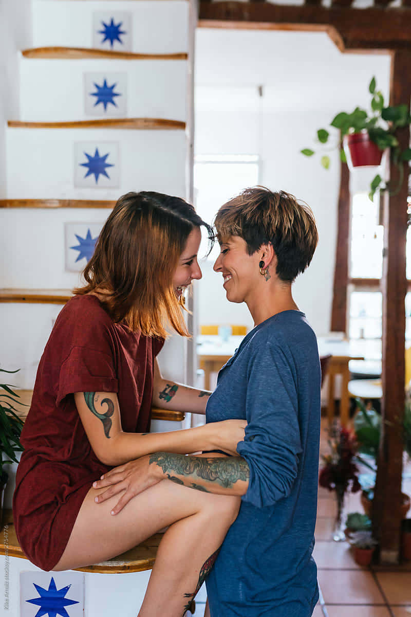 兩位紋身女性在室內裝飾的樓梯上微笑擁抱。