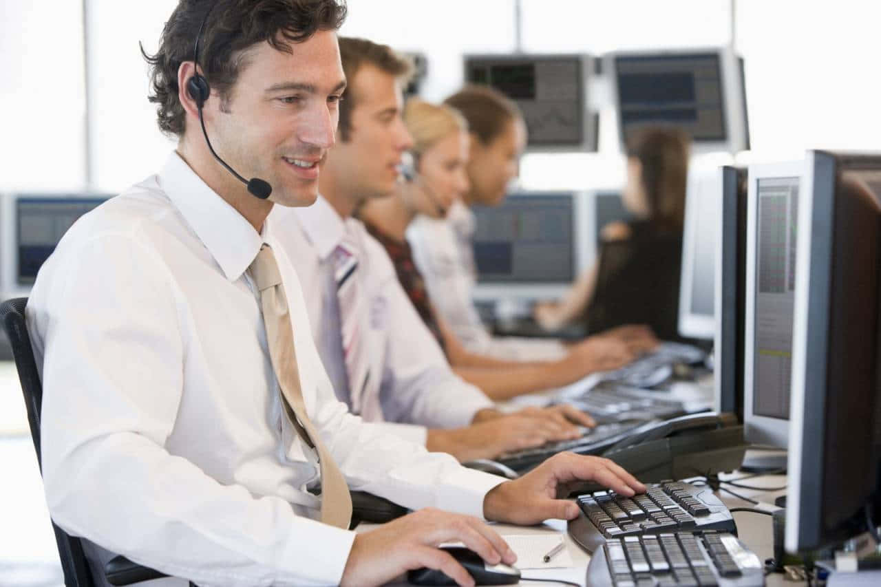 Telemarketing 桌布 壁紙 — 微笑的客戶服務代理穿著白襯衫和領帶，在明亮的呼叫中心的電腦工作站工作。