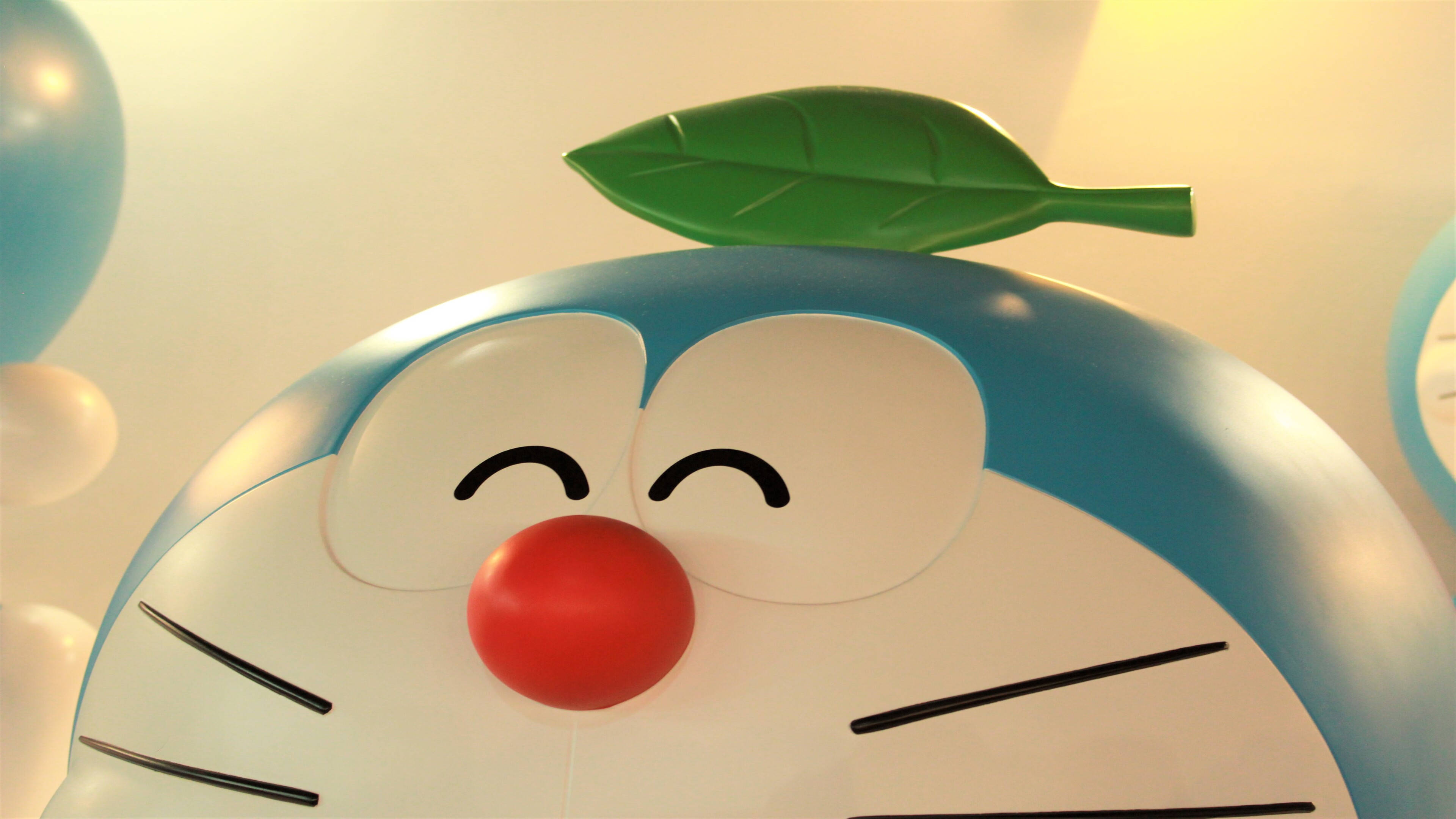 Doraemon 桌布 壁紙 — 微笑的藍色機械貓特寫，頭上有一片綠葉，柔和溫暖的燈光。