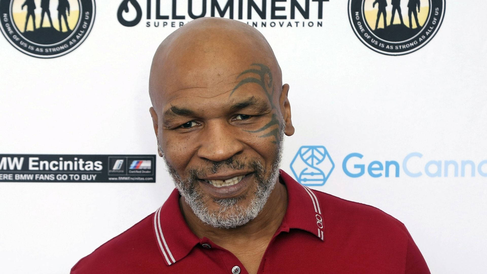 微笑的邁克·泰森 壁紙 — Mike Tyson 穿著紅色Polo衫，在品牌活動背景前溫暖地微笑。