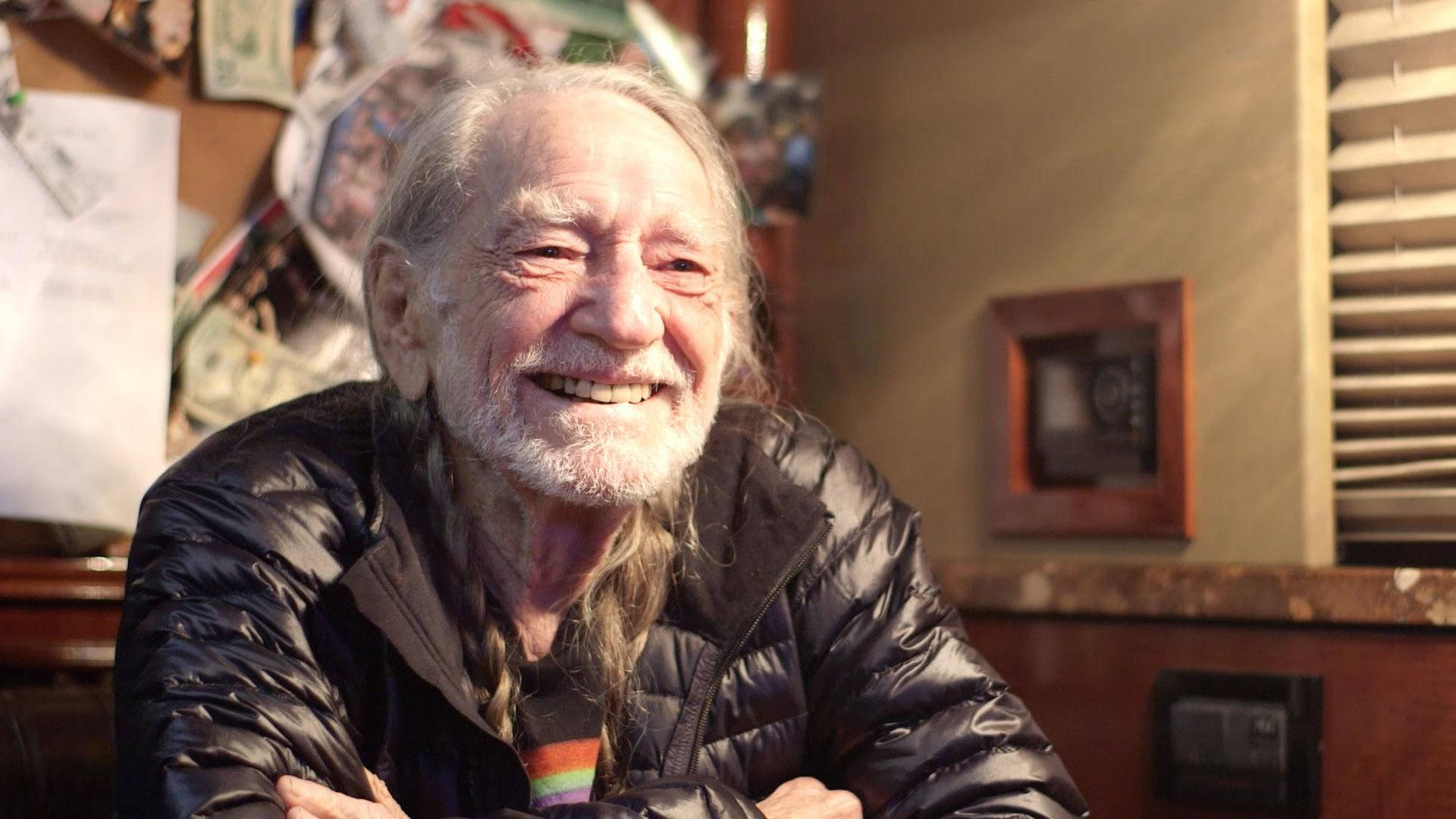 一位留著白鬍子和長髮的長者，在舒適的家居環境中露出溫暖的笑容。