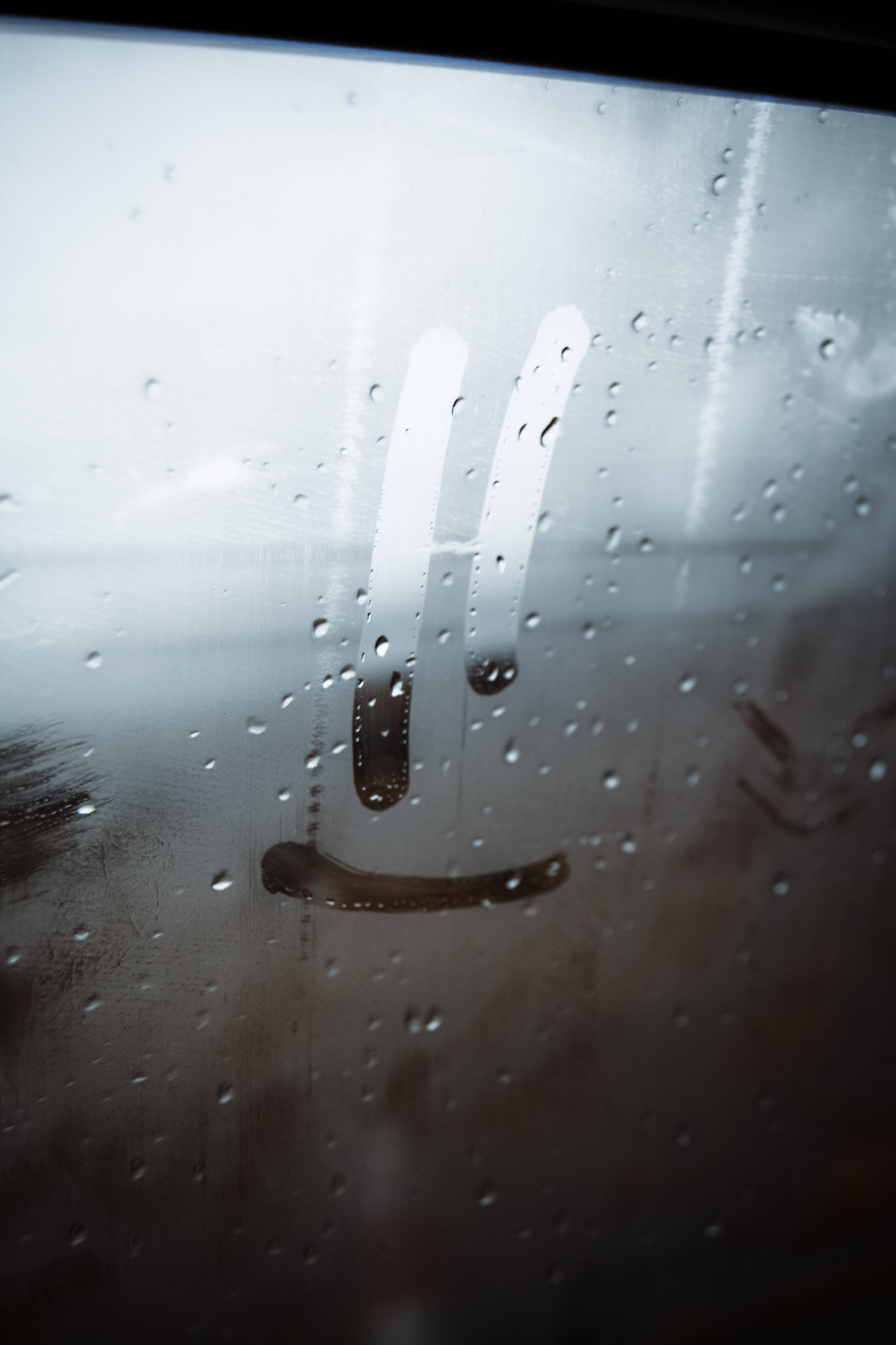 微笑臉美學鎖屏 壁紙 — 玻璃門上雨滴的特寫，上面畫著一個模糊的笑臉，營造出一種陰鬱而內省的氛圍。