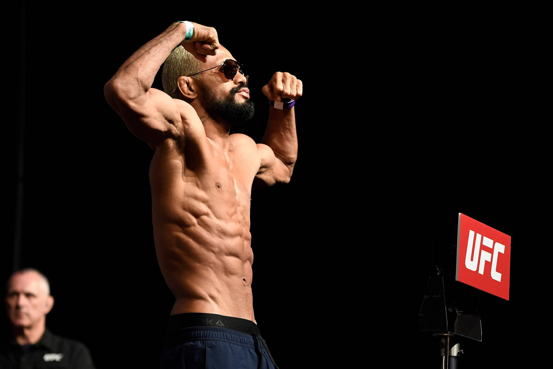 赤裸上身的戰士在紅色標誌的UFC舞台上繃緊肌肉。