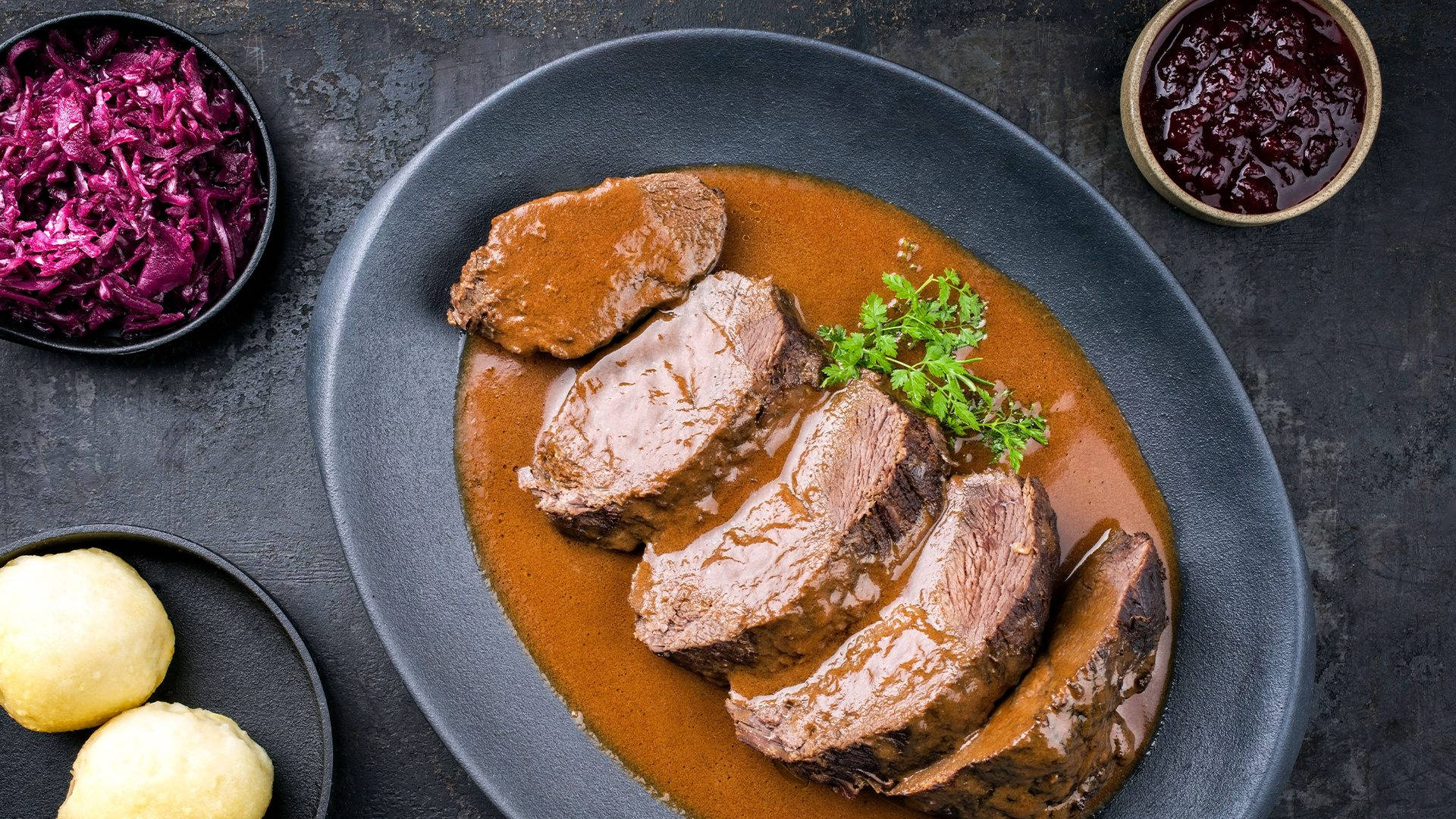 深色碟上的切片牛肉配肉汁和配菜。