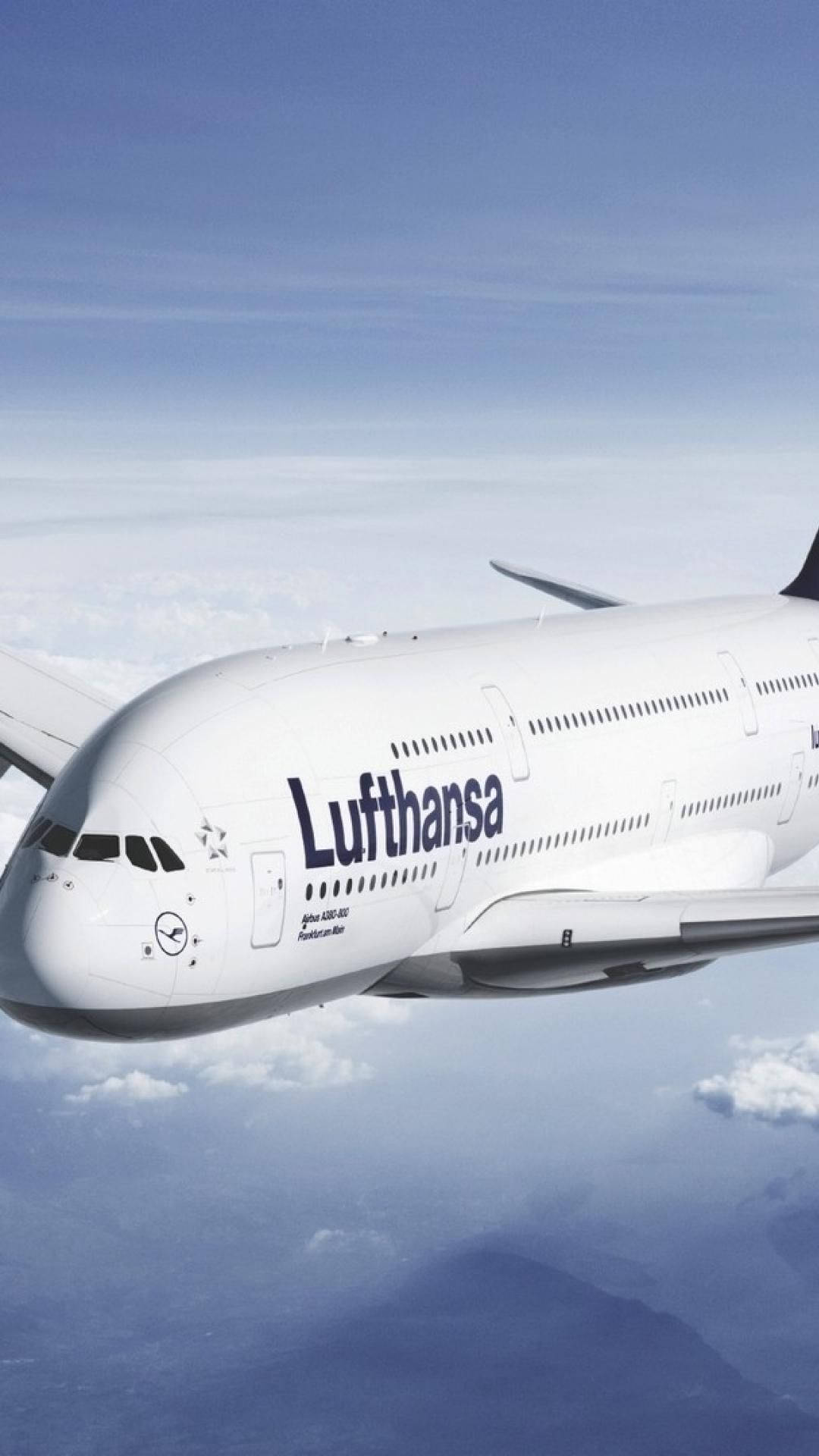漢莎航空空中巴士A380在雲層上方飛行，遠方有山脈。