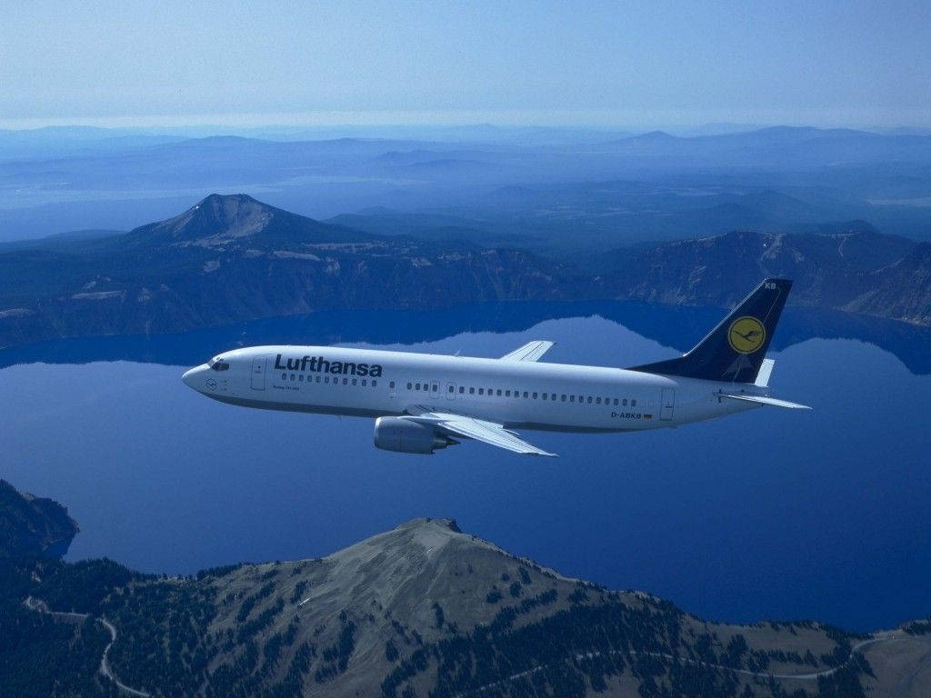 漢莎航空飛機飛越山間湖泊，天空清澈湛藍
