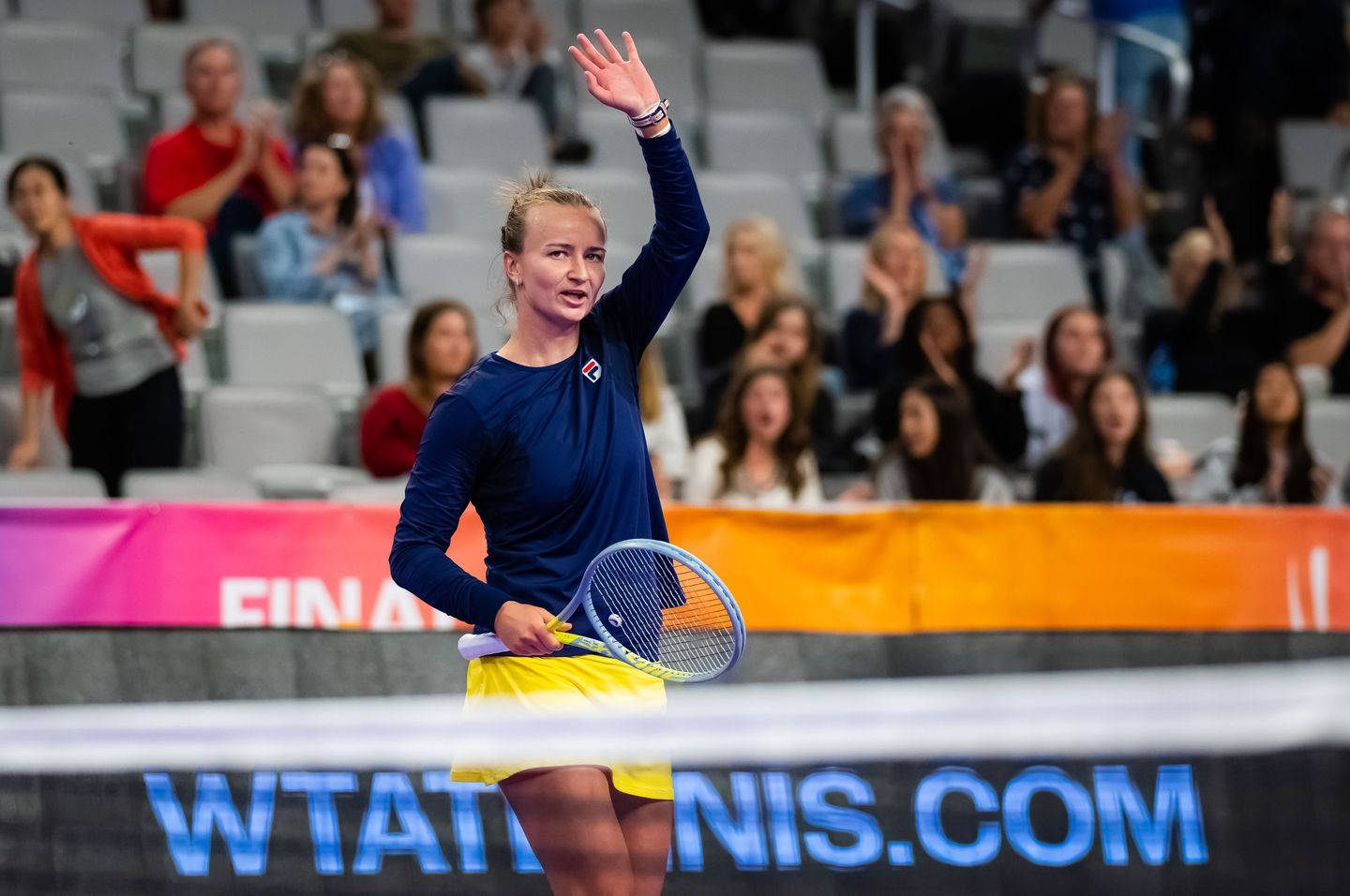 德州WTA總決賽巴博拉·克雷奇科娃 壁紙 — 一位女網球手在帶有 'WTATENNIS.COM' 標誌的球場上，手持球拍向歡呼的球迷揮手。