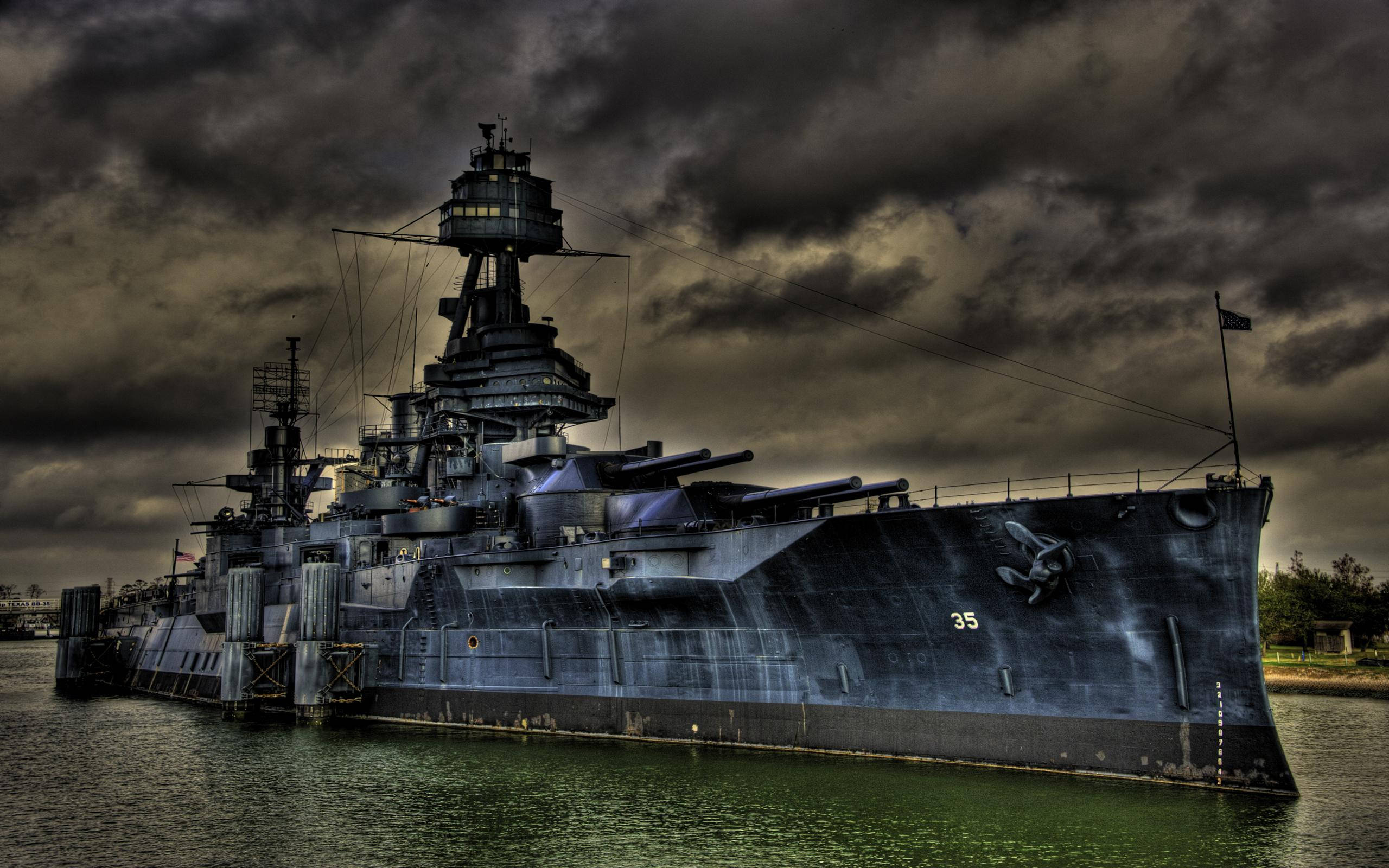 德州戰艦 USS Texas 壁紙 — 一艘擁有炮塔和編號35的巨大戰艦，在暴風雨灰暗的天空下，停泊在渾濁的水中。