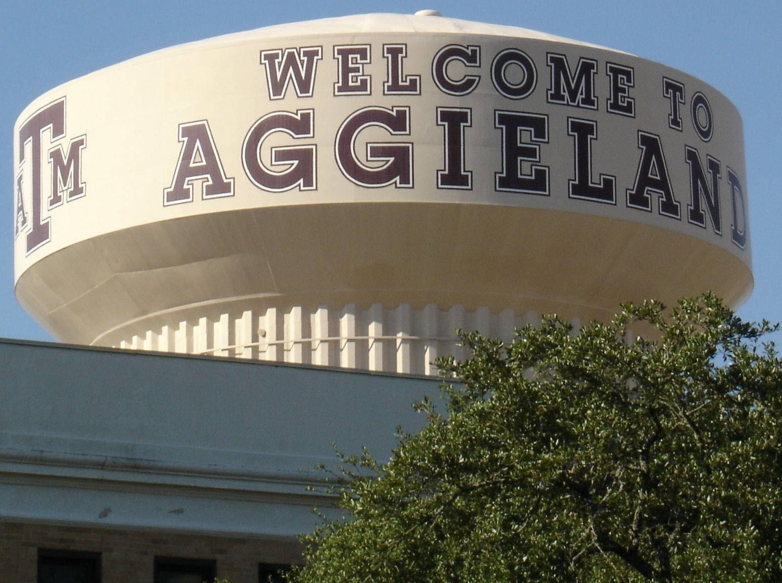 水塔，上面有 'Welcome to Aggieland' 字樣，下方有綠色樹木