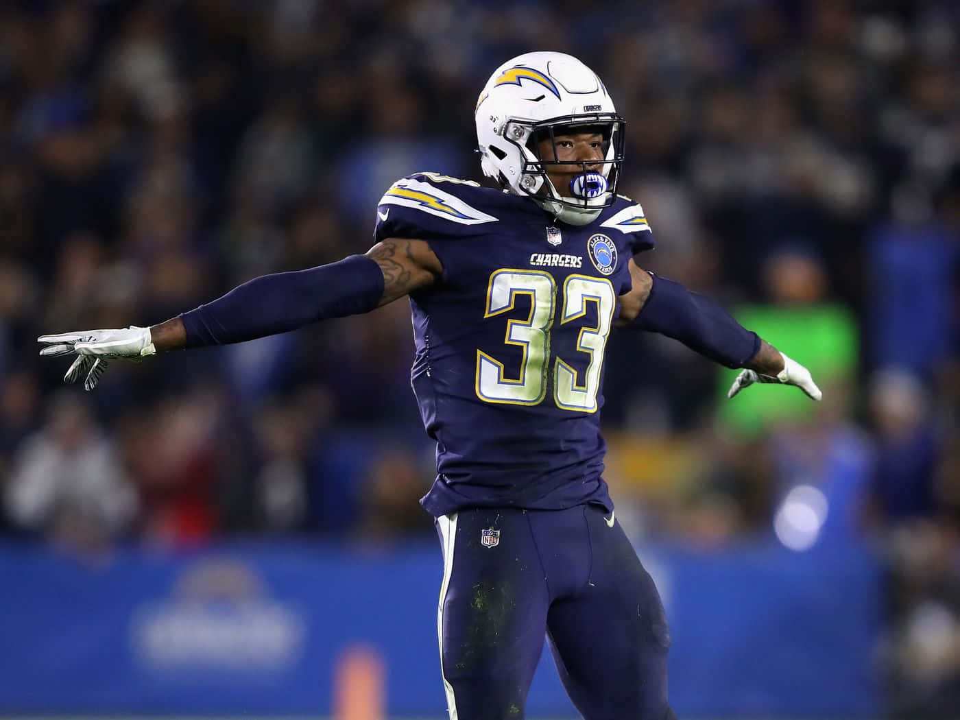 德文·詹姆斯 洛杉磯chargers 安全衛 壁紙 — 一位身穿紫色33號球衣的Chargers美式足球員在球場燈光下張開雙臂慶祝。