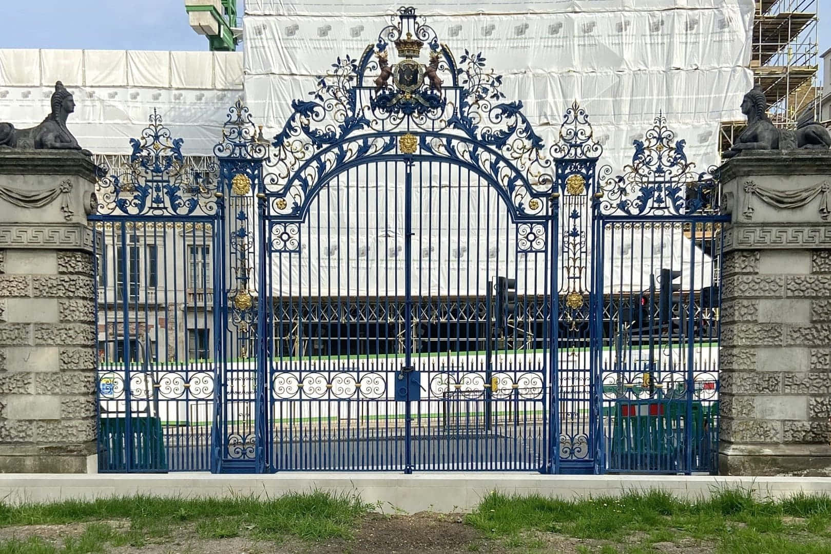 德文郡宅邸俯瞰綠園 壁紙 — 一座帶有金色點綴和石柱的華麗藍色鍛鐵大門，矗立在白色棚架下的建築物前。