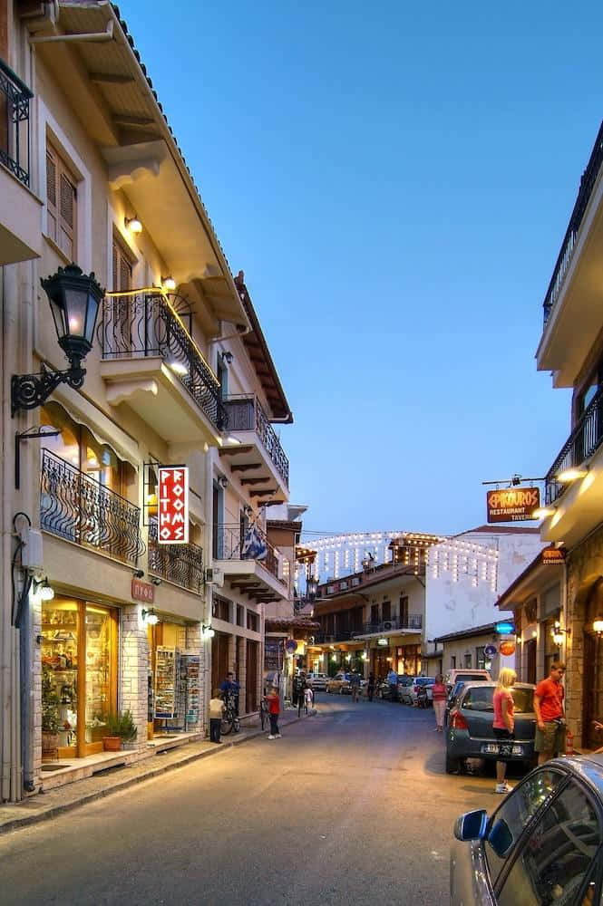 一條狹窄的街道，兩旁是燈火通明的商店和陽台，在暮色中。