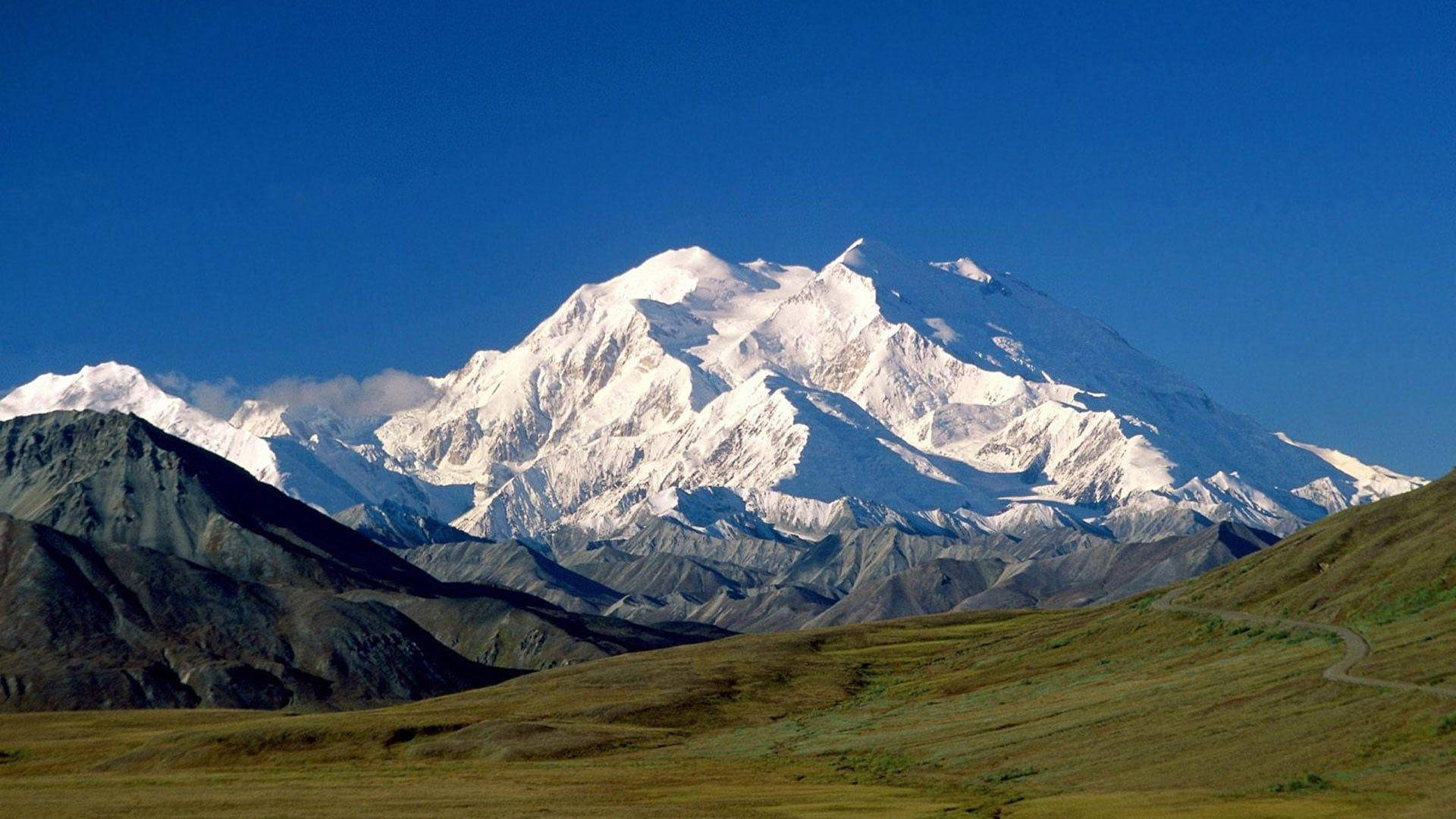 清澈藍天下的雪山峰頂，前景有蜿蜒的道路
