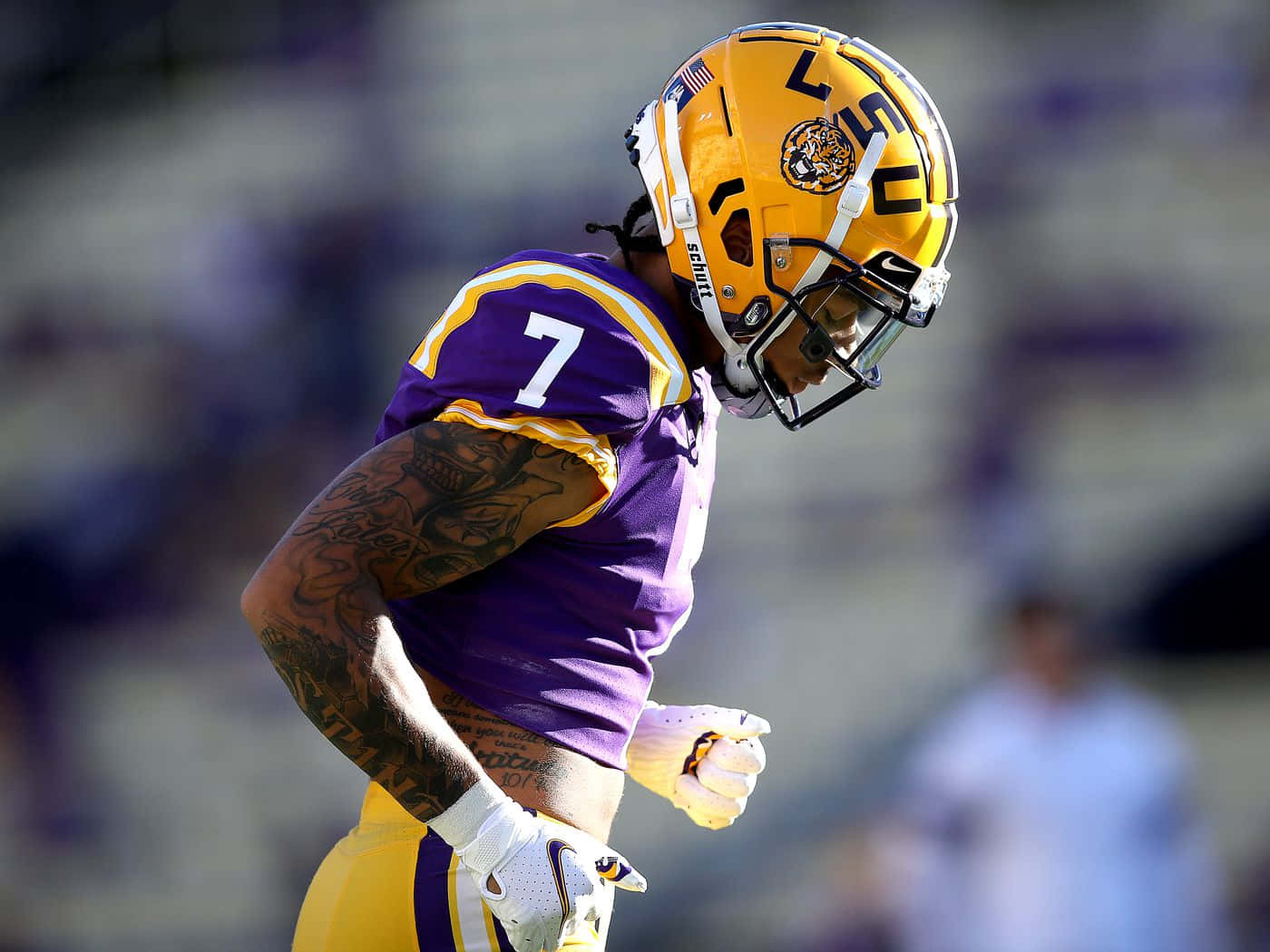 德里克·斯廷格利 Jr. NFL 球隊選秀第三順位 壁紙 — 一名身穿紫色和金色球衣、背號7的LSU美式足球員在比賽中低頭，露出有紋身的手臂。