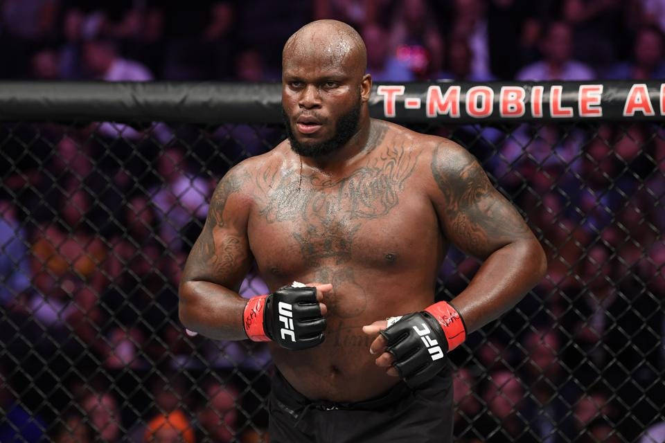 一位有紋身的肌肉發達MMA拳手，戴著紅黑手套，站在UFC八角籠內。