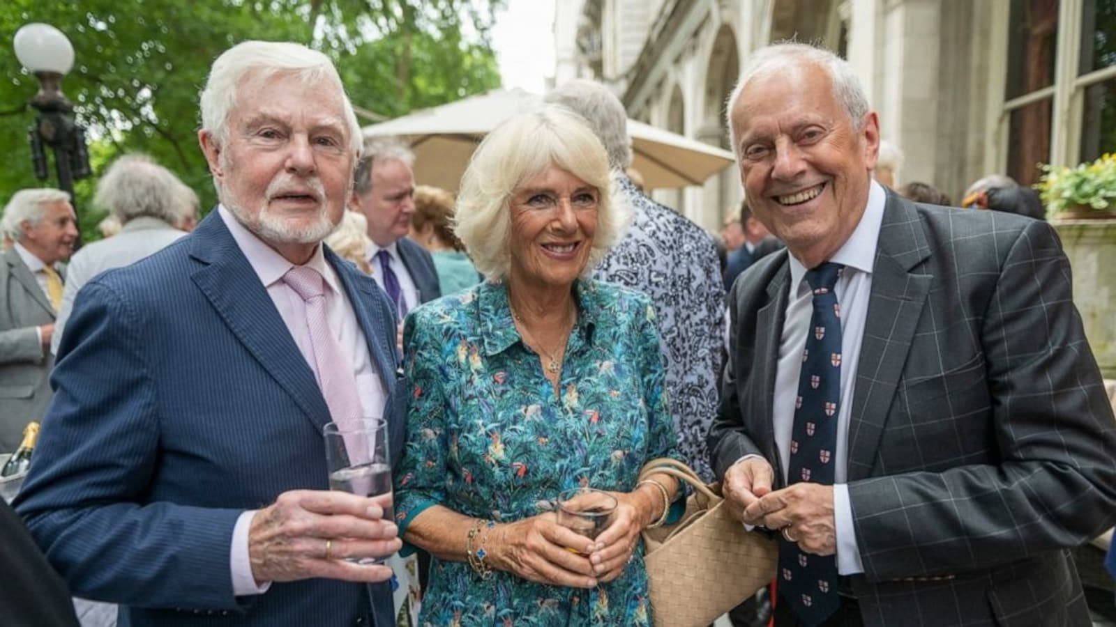 德里克·雅各比與英國王后 Consort Camilla 壁紙 — 三位微笑的長者穿著正式服裝，在日間社交聚會中一起於戶外擺姿勢。