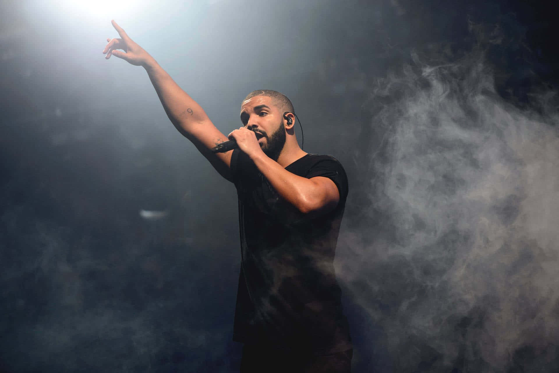 Drake 在聚光燈下煙霧繚繞的舞台上對著麥克風唱歌。