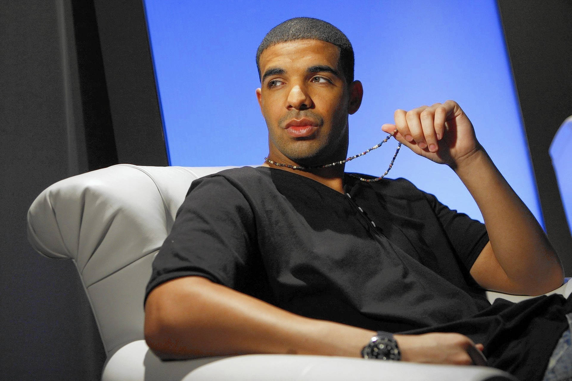 Drake 在訪問中坐在白色椅子上手持珠鏈。