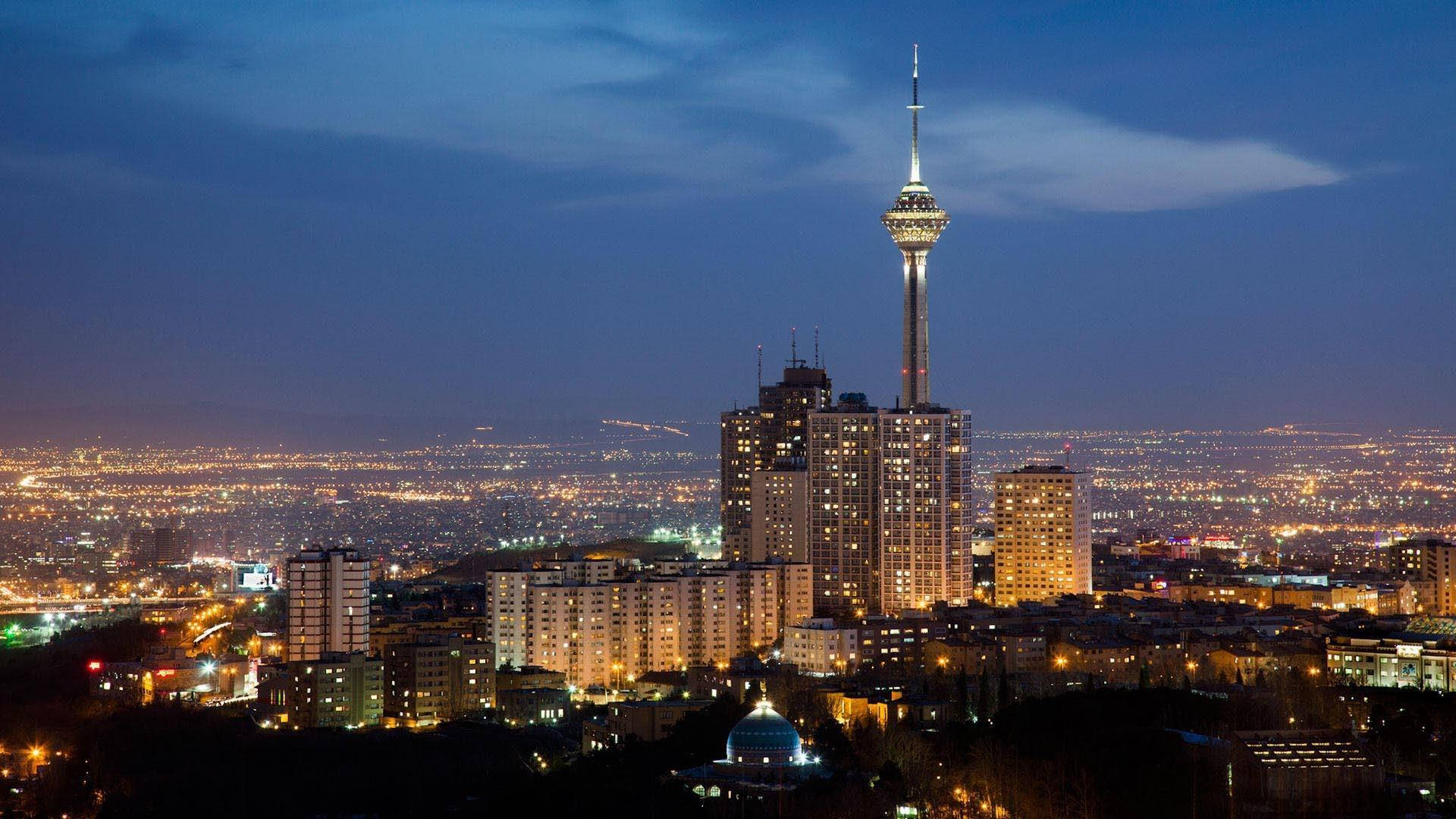 德黑蘭商業區 壁紙 — 德黑蘭天際線的 panoramic 夜景，以燈火通明的米拉德塔和深藍色天空下蔓延的城市燈光為主導。
