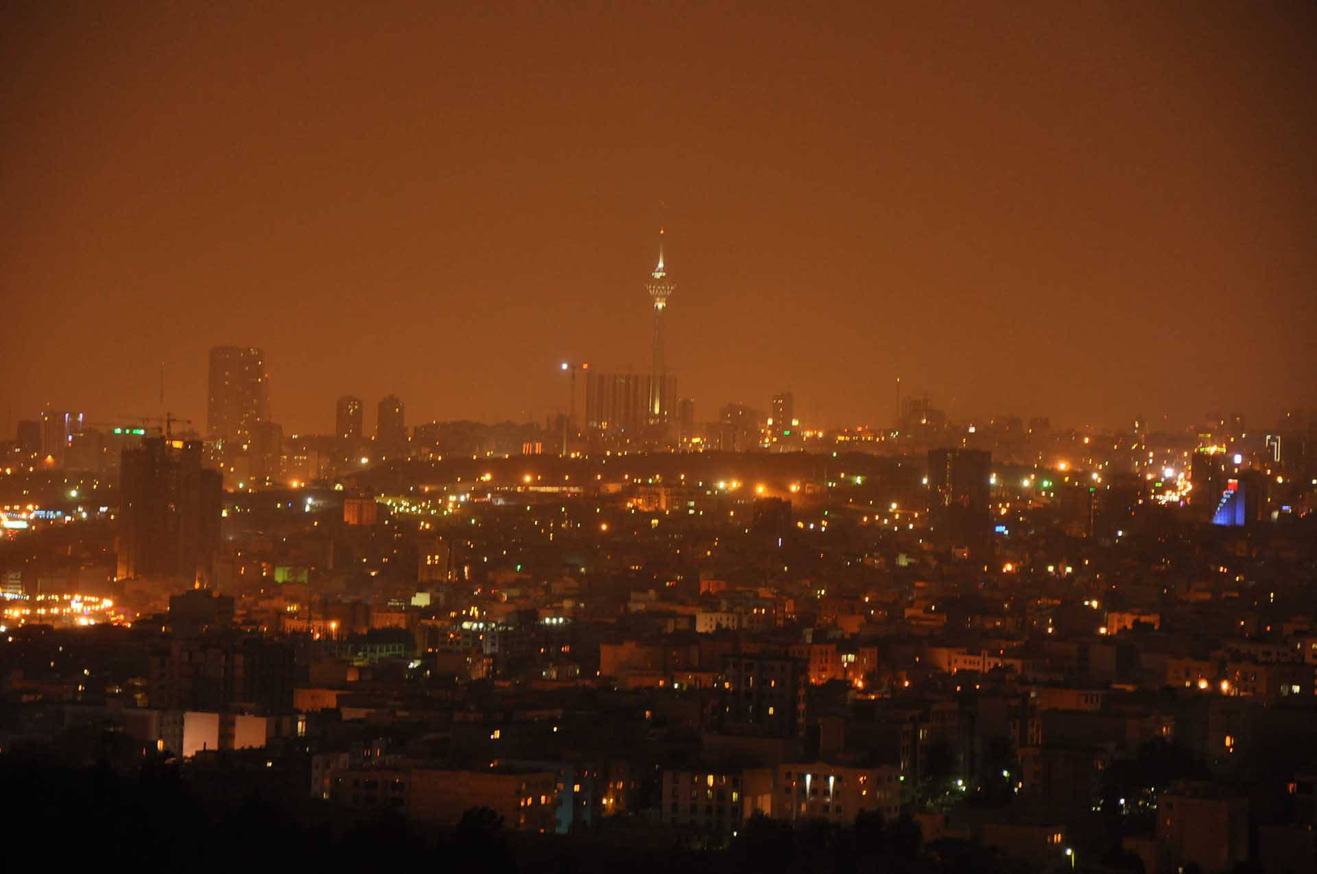 德黑蘭橙色濾鏡夜景 壁紙 — 朦朧的夜景城市景觀，無數建築物和一座高聳的中央尖塔散發出溫暖的橙色光芒。