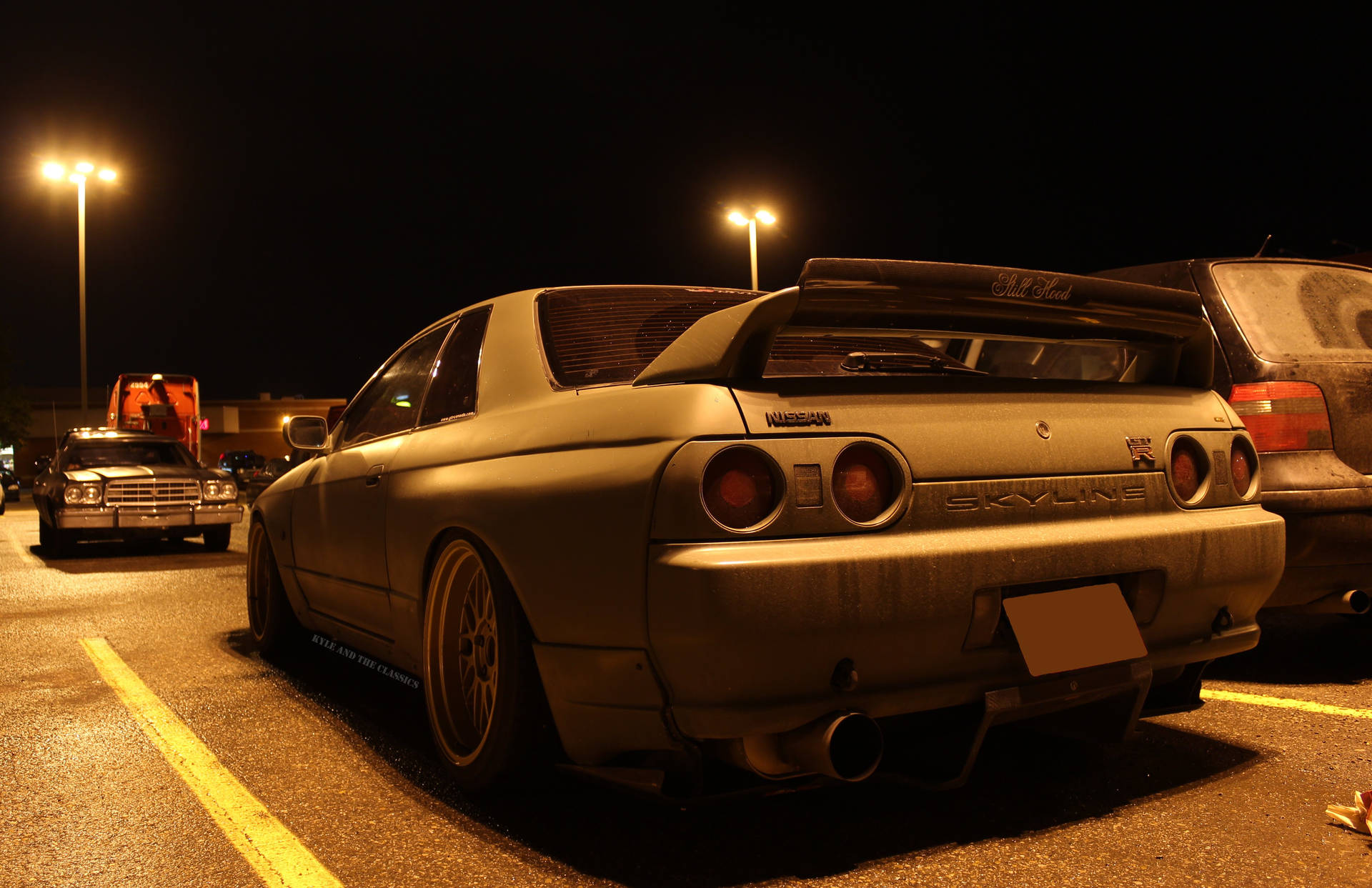 一架啞光灰色日產Skyline R32在夜晚停泊在停車場的街燈下。