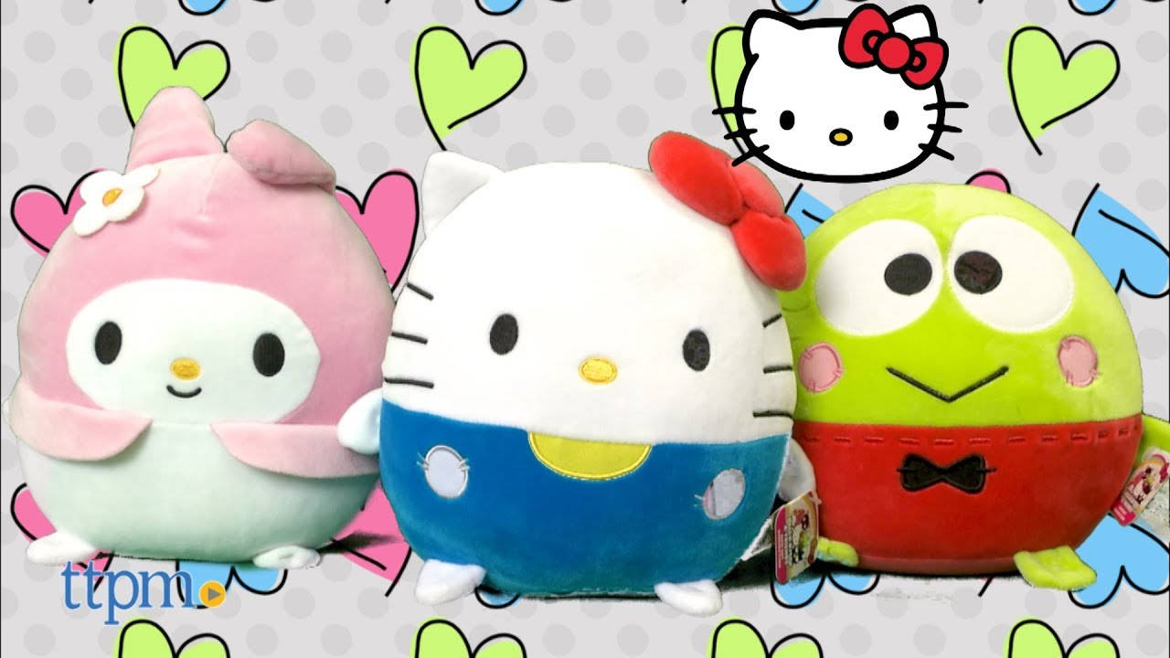 心形圖案背景的Squishmallows 壁紙 — 三個可愛毛絨玩具 My Melody Hello Kitty 和 Keroppi 一起坐在心形圖案背景前。