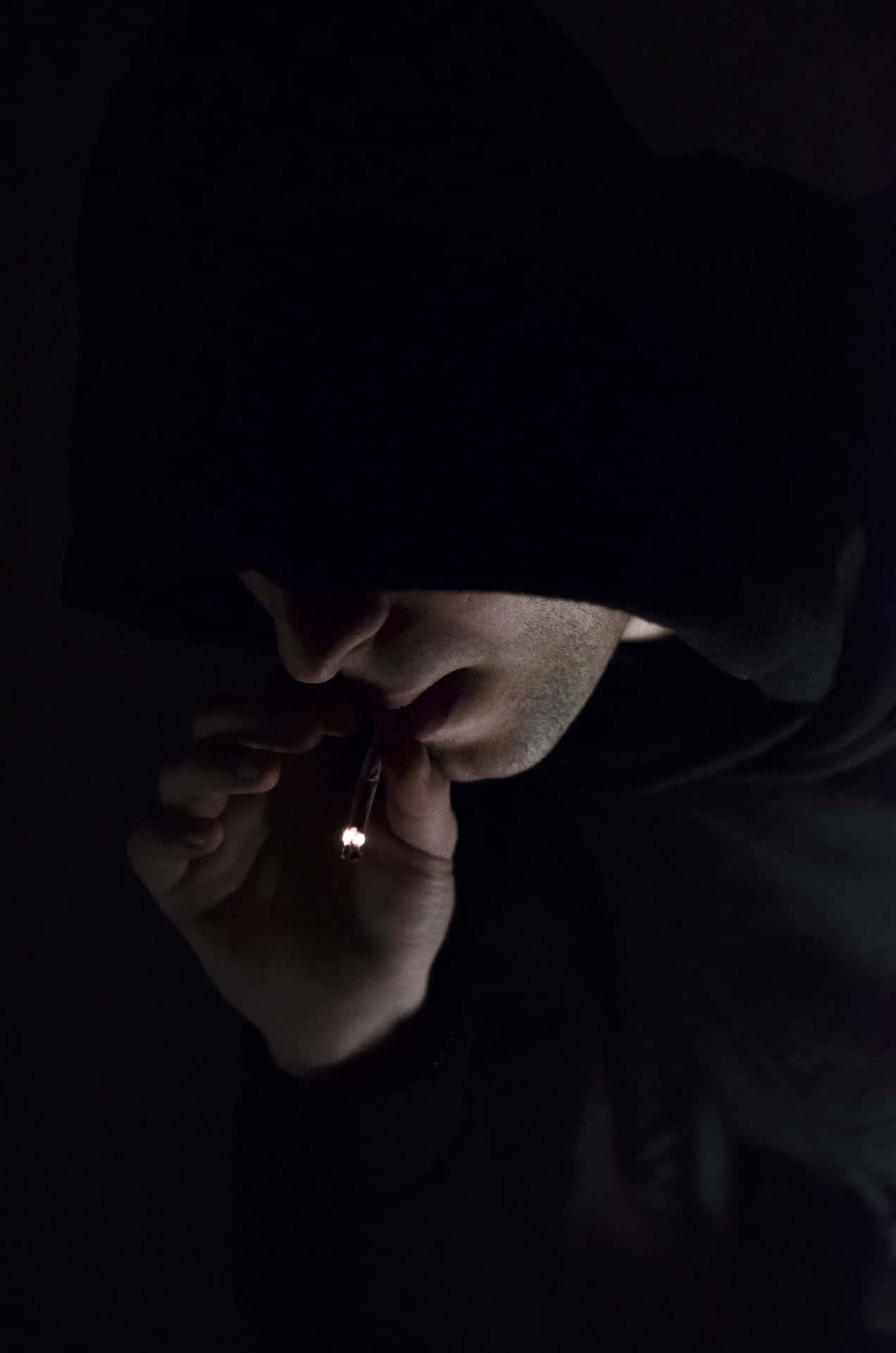 穿著深色連帽衫的人在昏暗光線下點煙