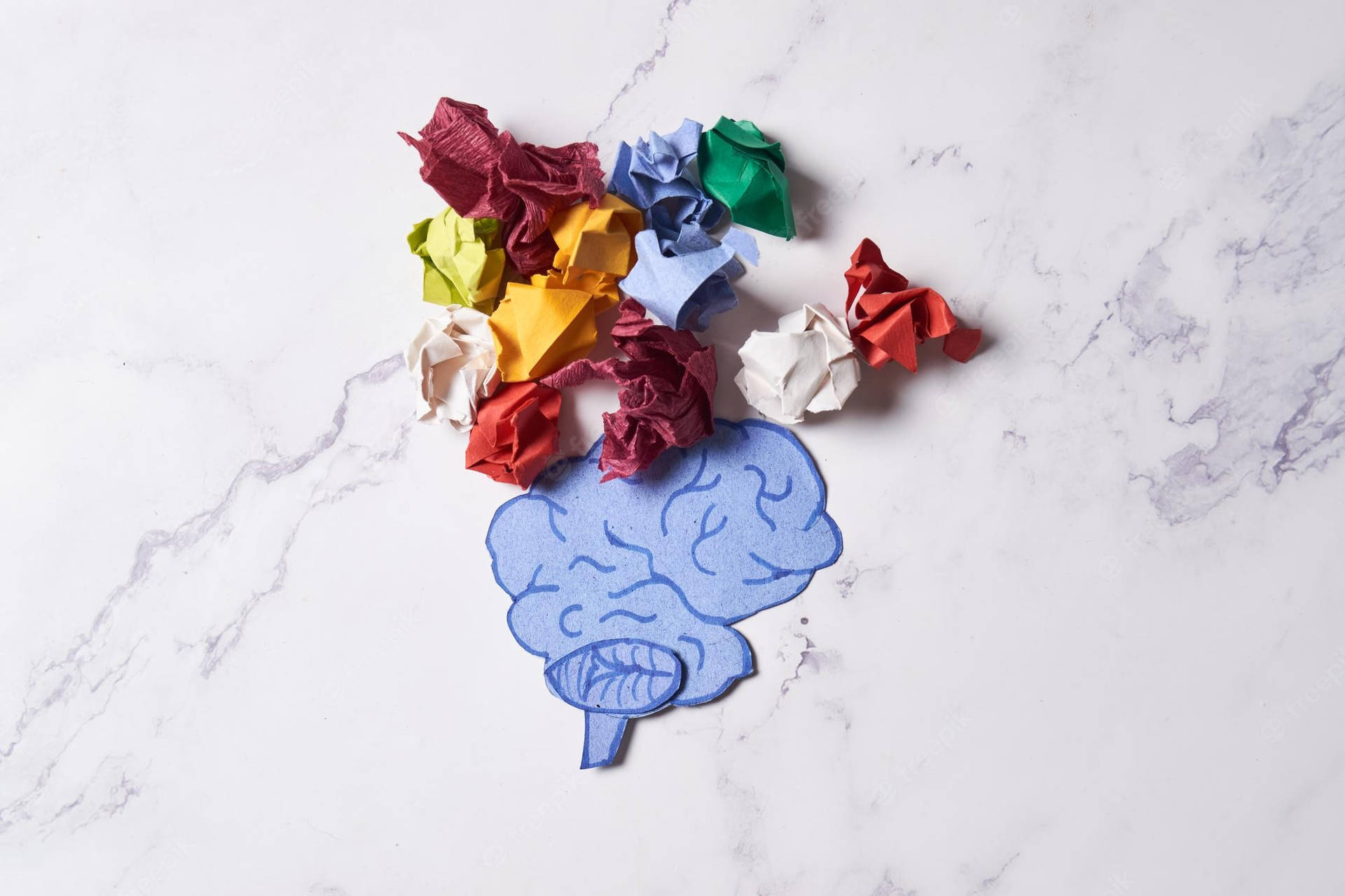 藍色紙質大腦剪紙，被彩色皺紙環繞，置於大理石上。