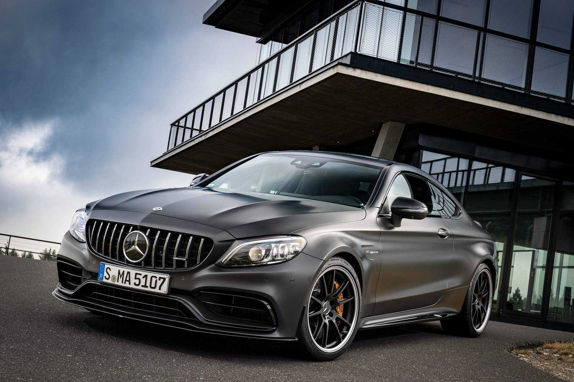 啞光灰色 Mercedes-AMG C63 S 雙門轎跑車停放在現代玻璃建築下。