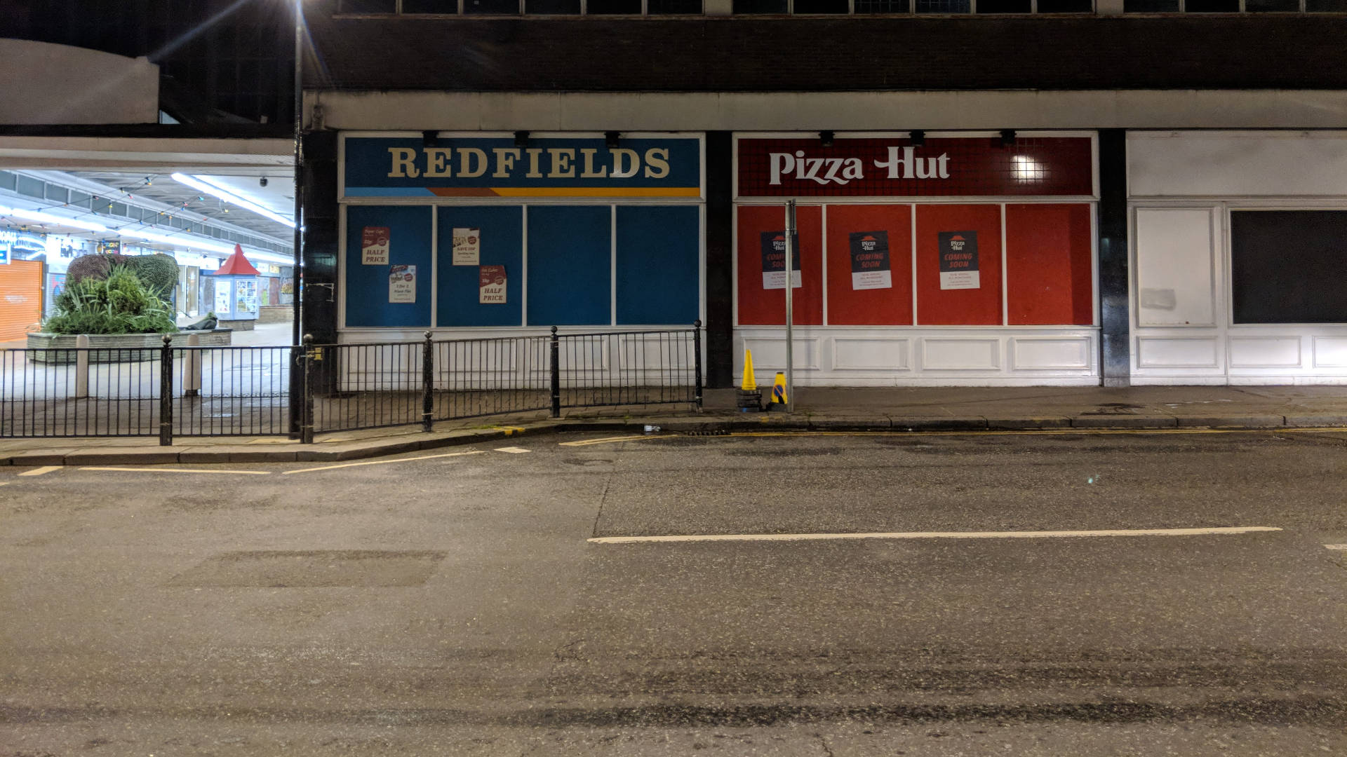 必勝客與Redfields商店夜景 壁紙 — 夜晚街景，關閉的Redfields和Pizza Hut店面在人工燈光下，路面濕滑。