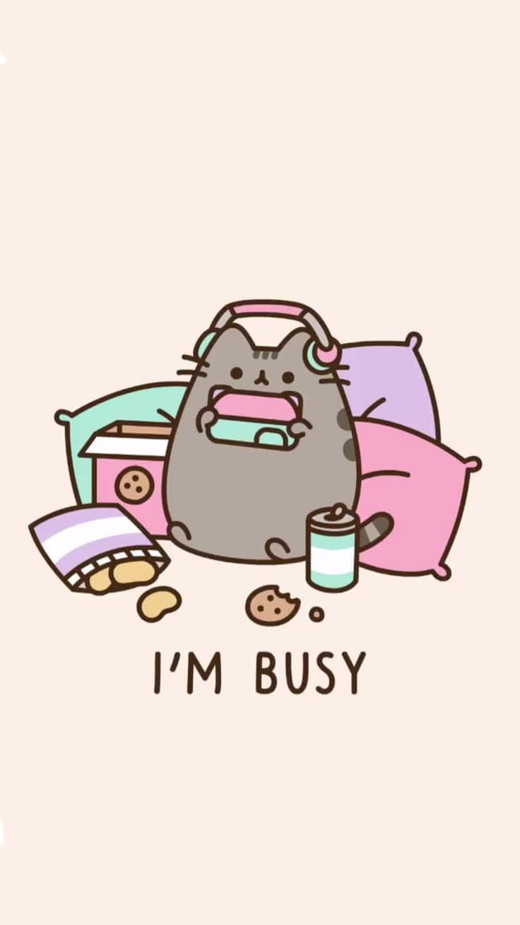 忙碌的 Pusheen 貓可愛遊戲玩家 壁紙 — 一隻戴著耳機的可愛灰色貓咪坐在枕頭、零食和飲料中間，拿著寫有「我很忙」的手機。