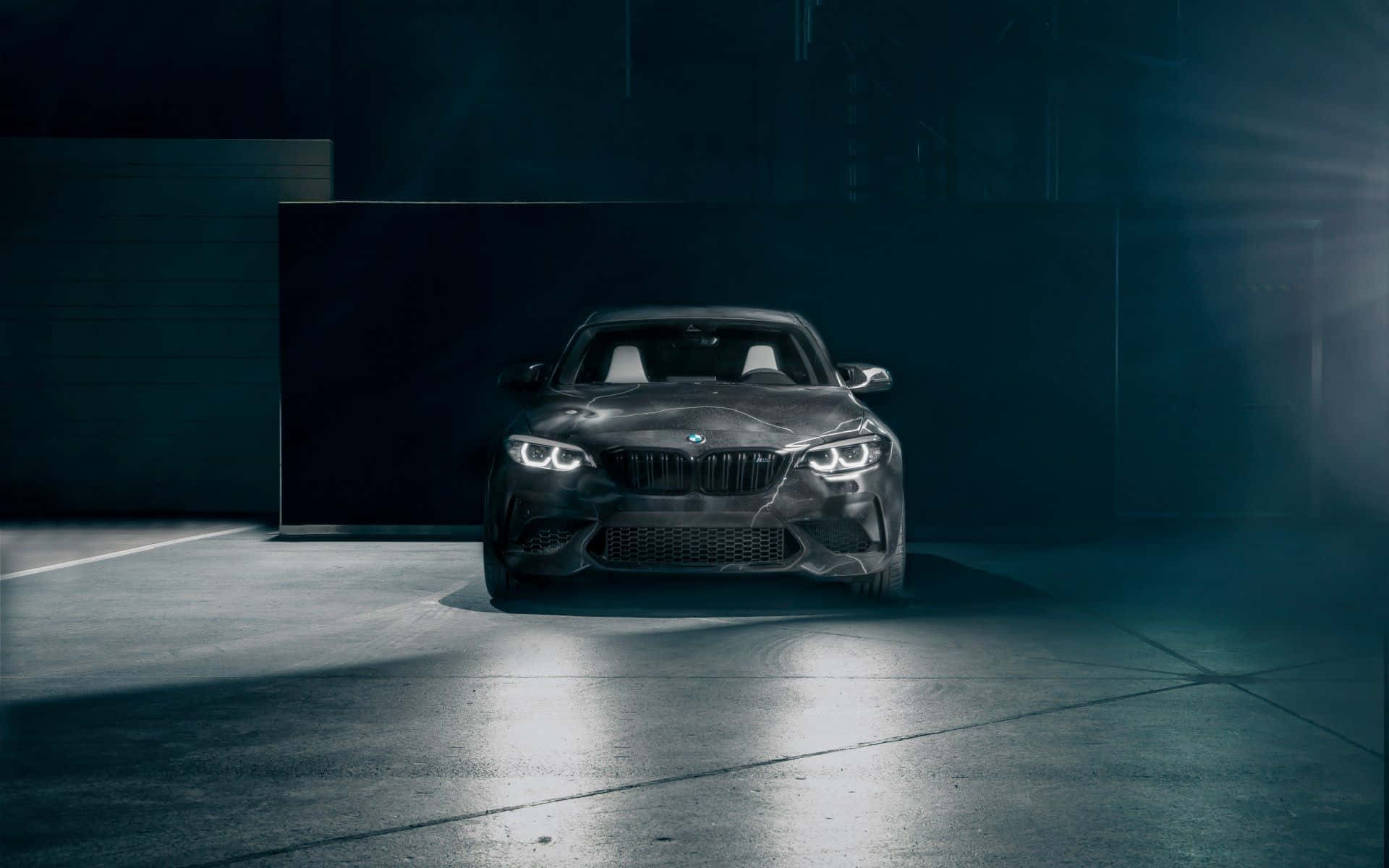 黑色BMW M2跑車在昏暗車庫中被聚光燈照亮，伴有薄霧。