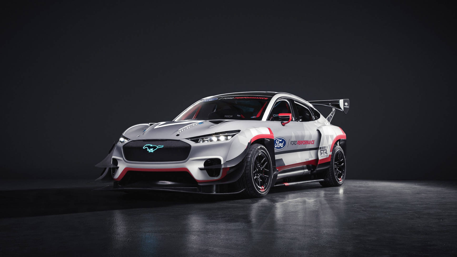 銀色福特野馬GT4賽車，帶有紅色點綴和發光的車頭燈，在黑暗的攝影棚中。