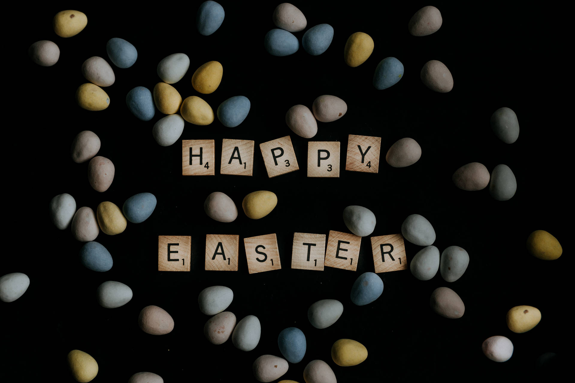 Happy Easter 用木磚拼出，黑色背景上圍繞著彩色蛋。