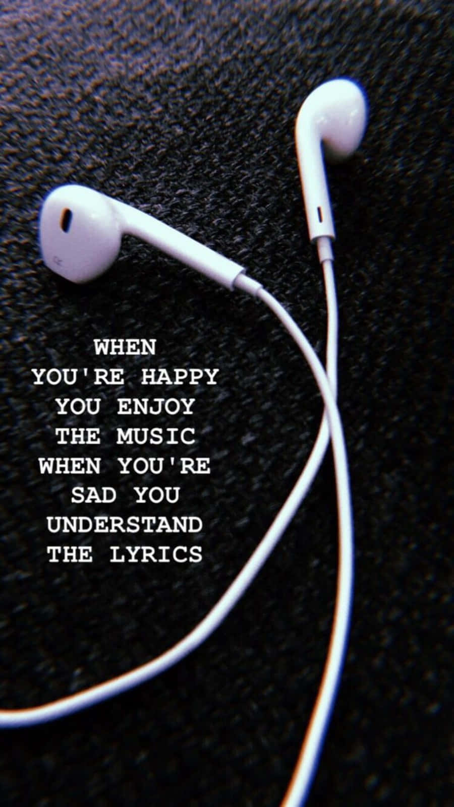 快樂時欣賞音樂，悲傷時理解歌詞 壁紙 — 白色耳機放在深色紋理布料上，疊加有關音樂和情感的文字。