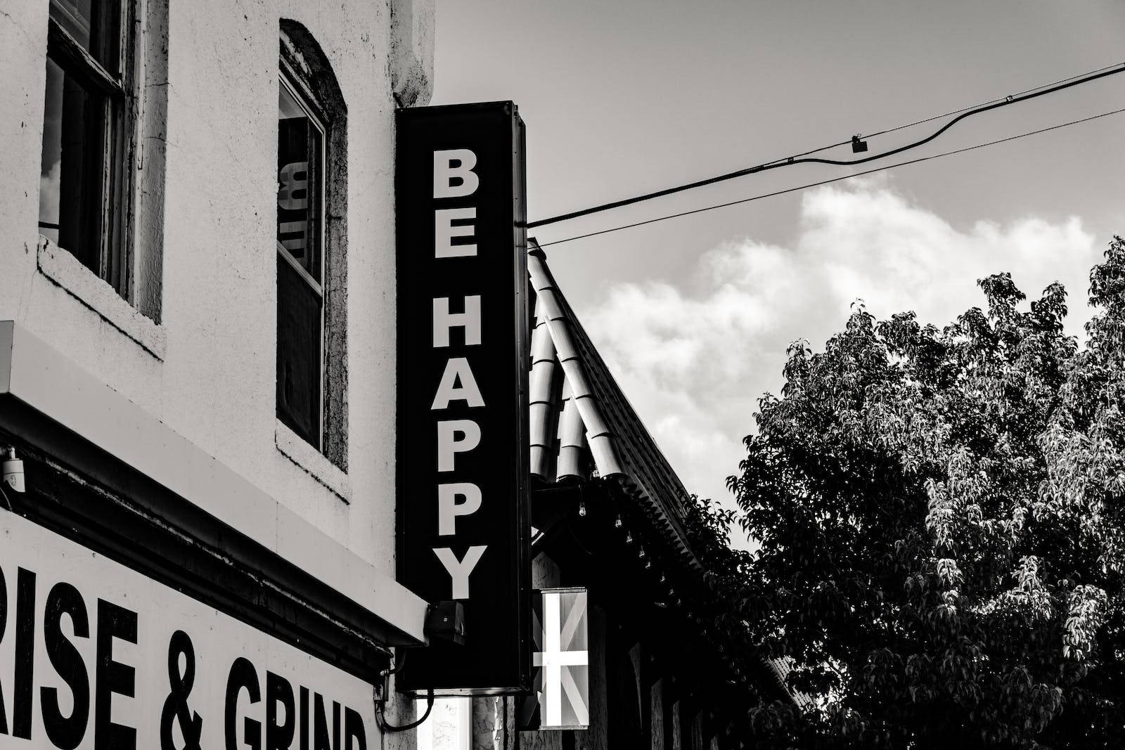 建築物上一個黑白標誌寫著「BE HAPPY」，背景有樹木和雲朵。