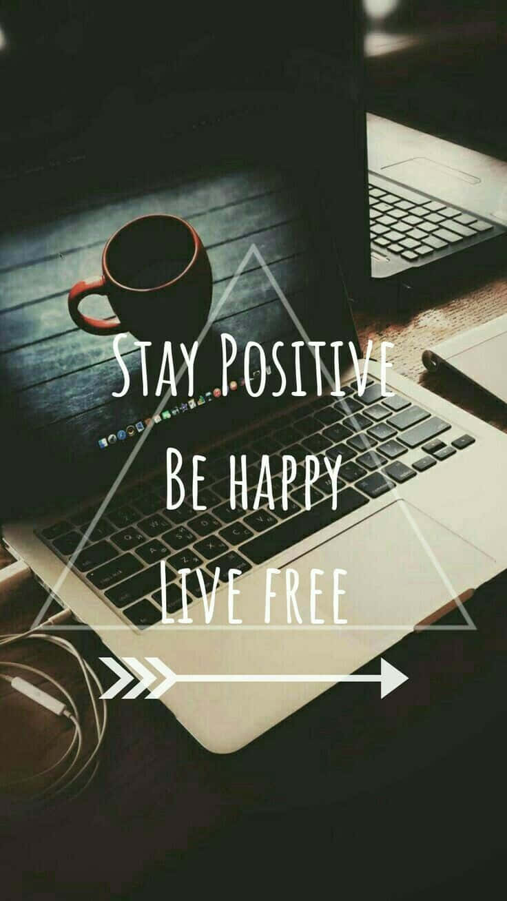 手提電腦屏幕顯示「Stay Positive Be Happy Live Free」，木桌上有咖啡杯。
