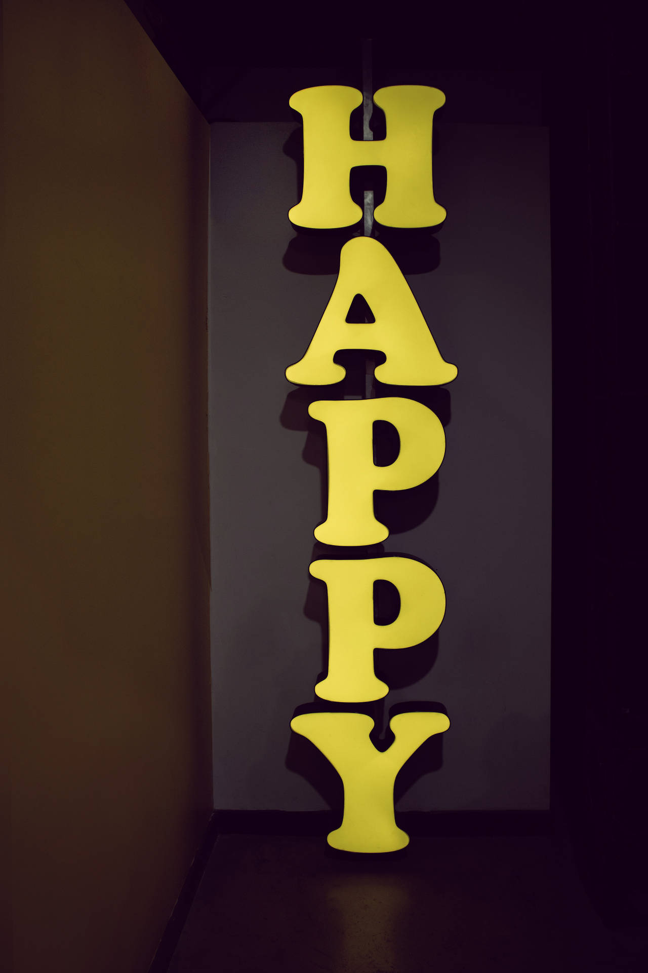 在黑暗的房間裡，一個黃色垂直霓虹燈牌拼寫著HAPPY。