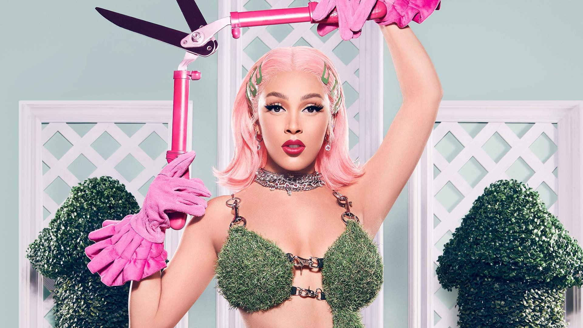 性感園丁 Doja Cat 壁紙 — 一位粉紅色頭髮、戴著粉紅色手套的女性，穿著苔蘚比基尼，在淺藍色格子背景前拿著巨大的粉紅色剪刀。